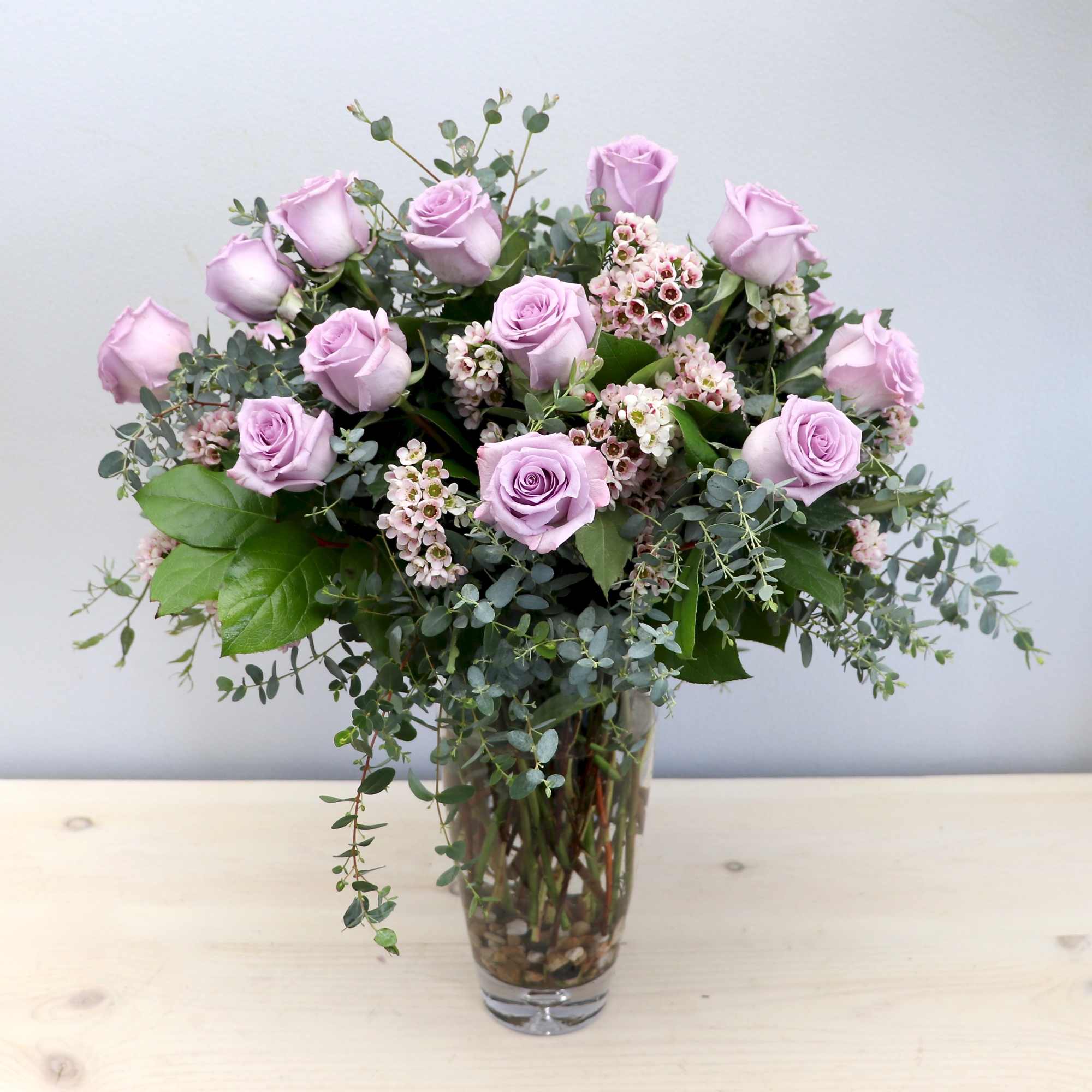 Tall arrangement of lavender roses and small pink blossoms in a clear glass vase