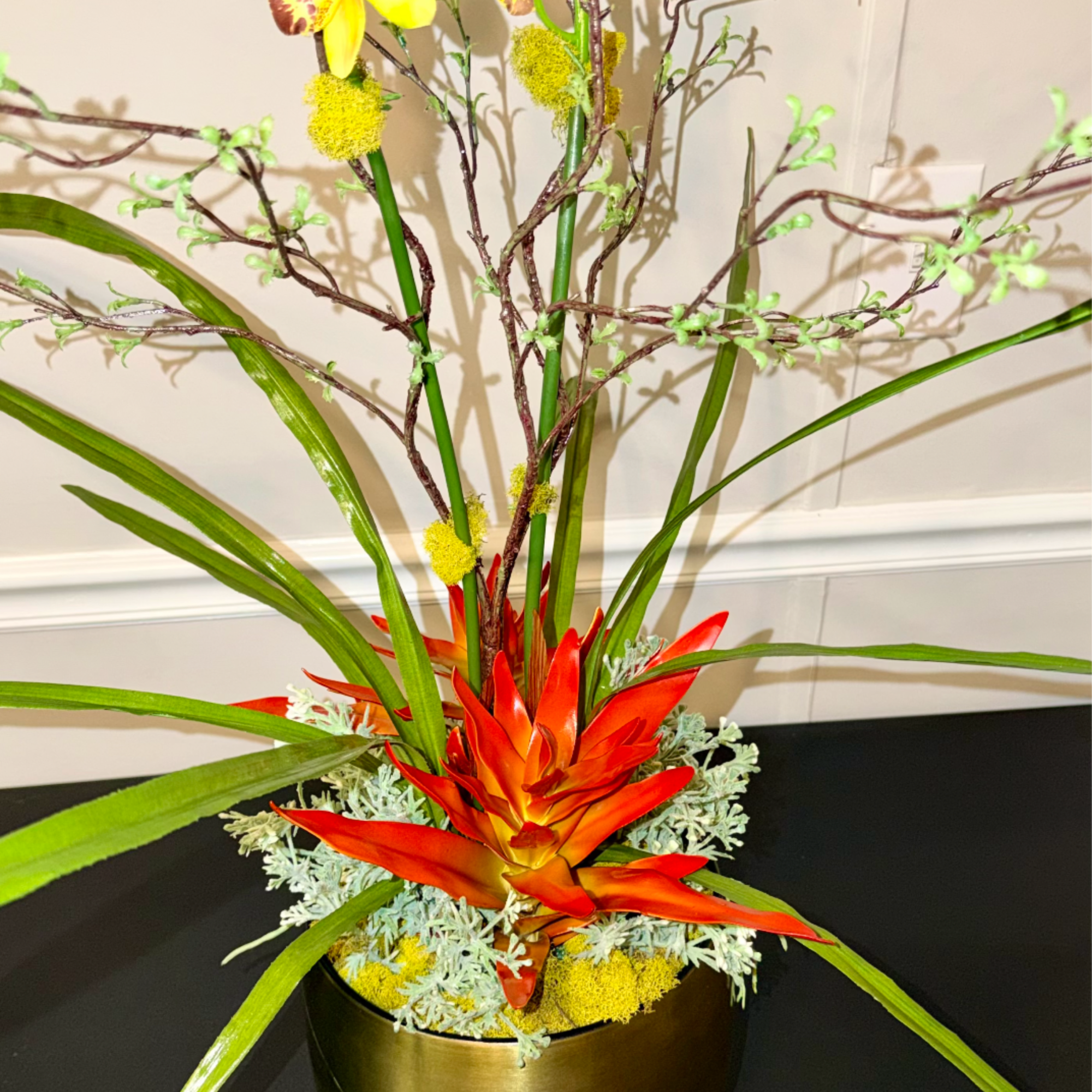 Tropical arrangement with orange bloom and tall yellow orchids in a gold footed pot