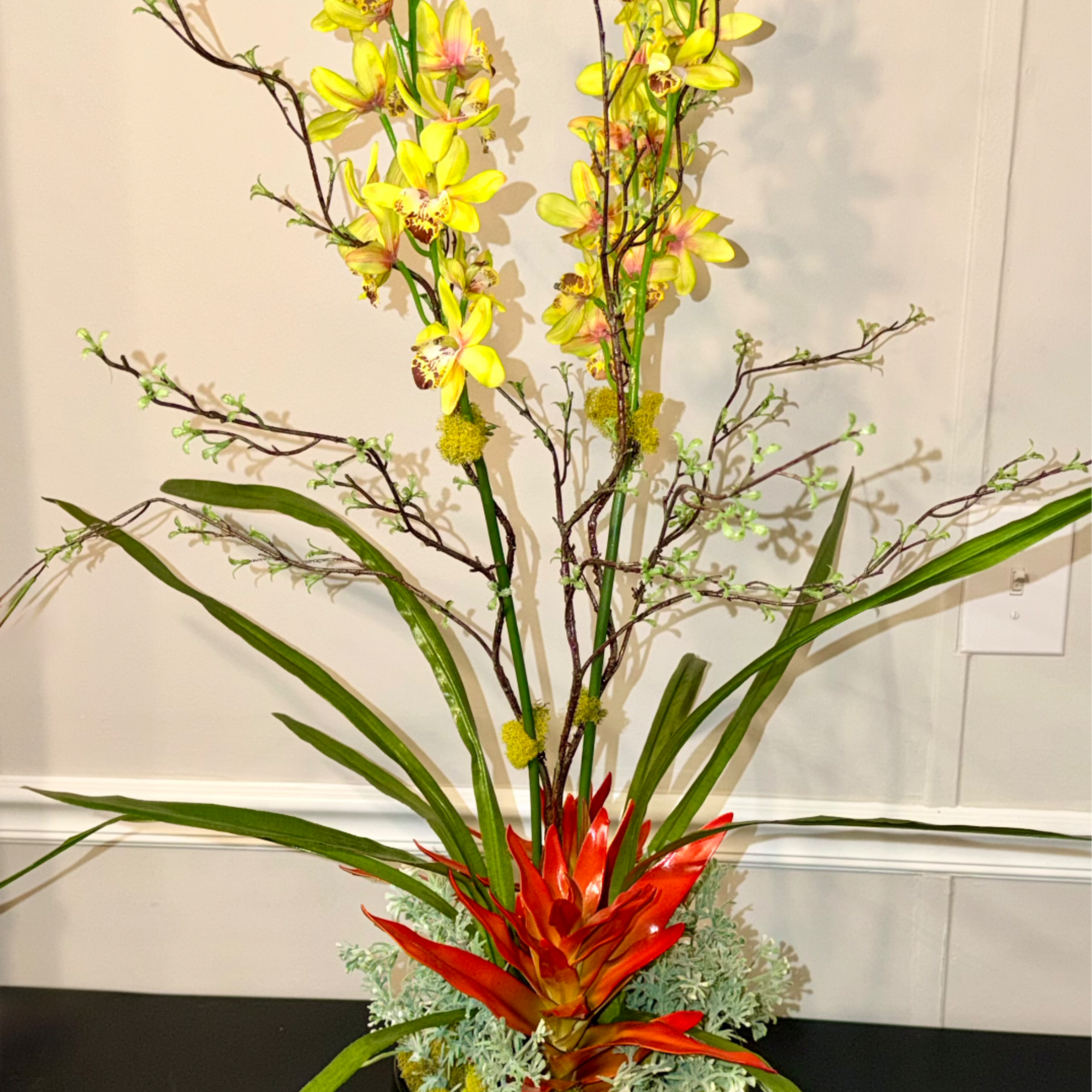Tall tropical arrangement with yellow orchids and red bromeliad in a gold pot