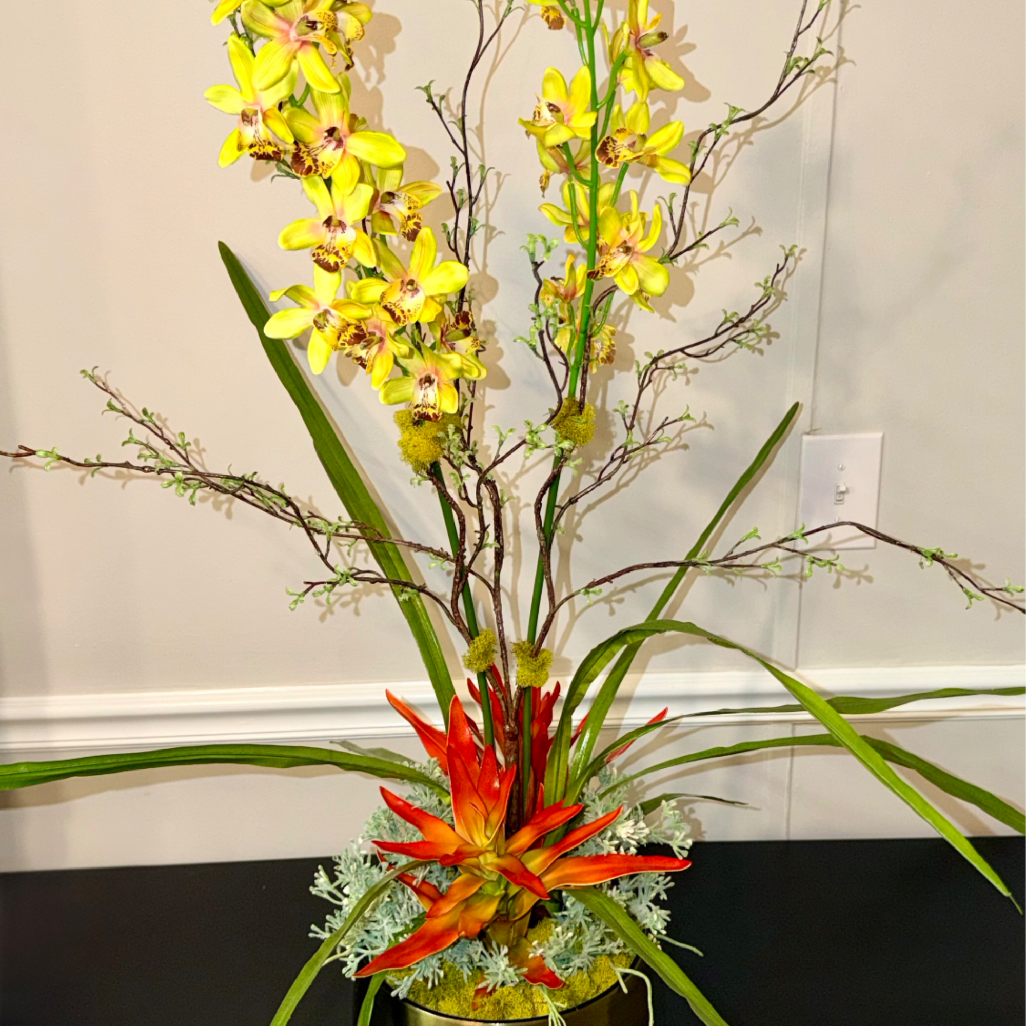 Tall arrangement with yellow orchids and an orange tropical flower in a gold pot