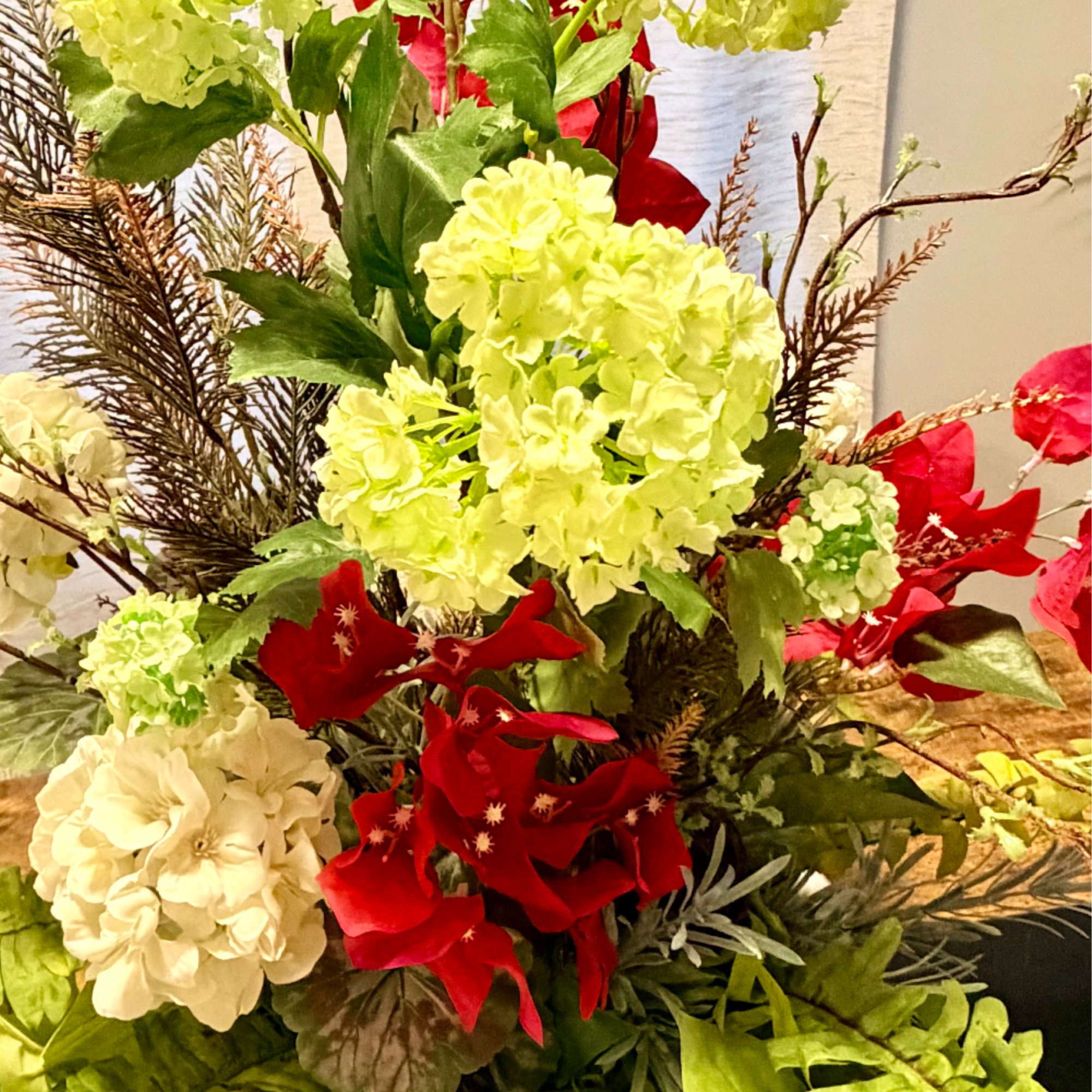 Tall arrangement of pale green and white hydrangeas with red blooms and fern fronds