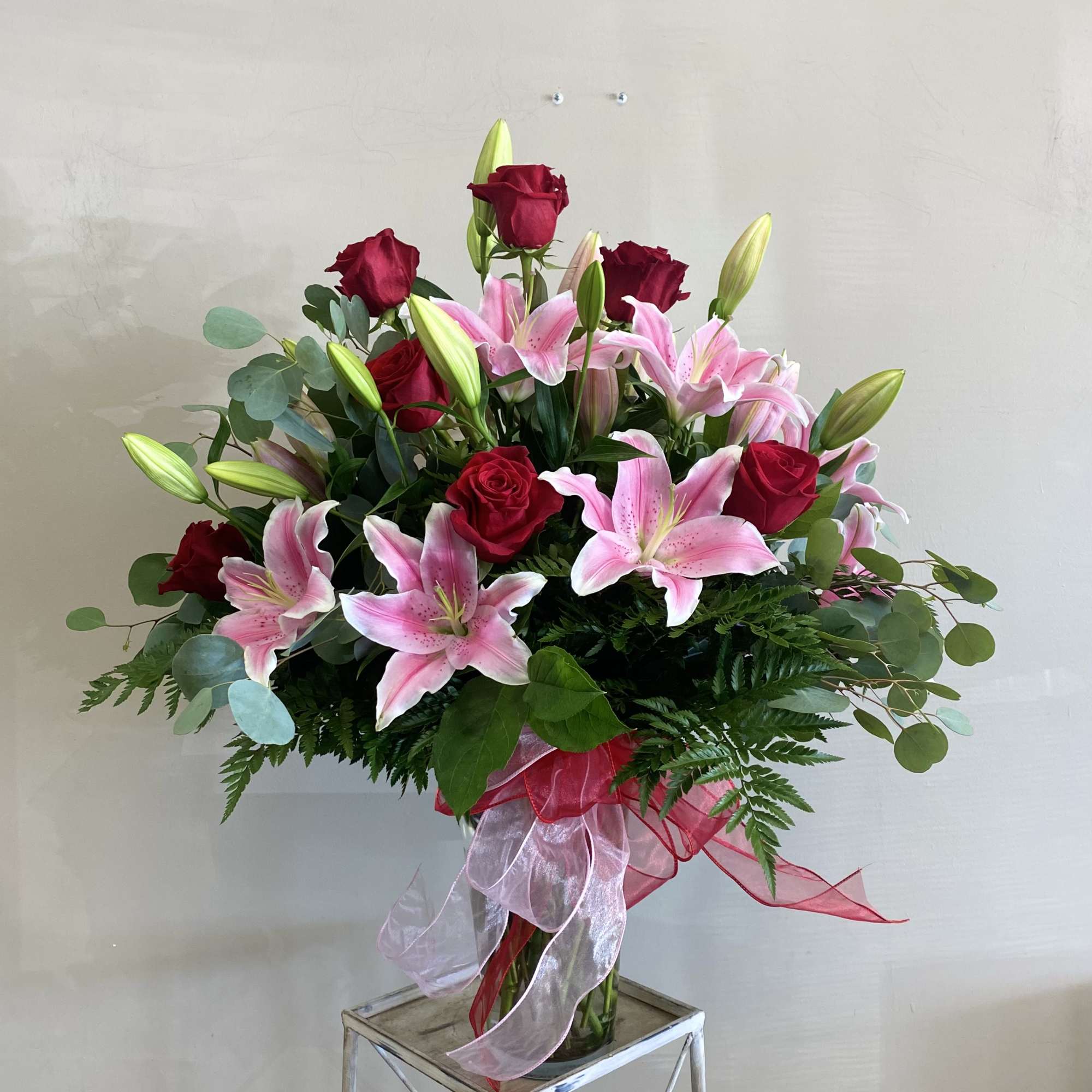 Tall arrangement of pink lilies and red roses in a clear vase with red and pink ribbon