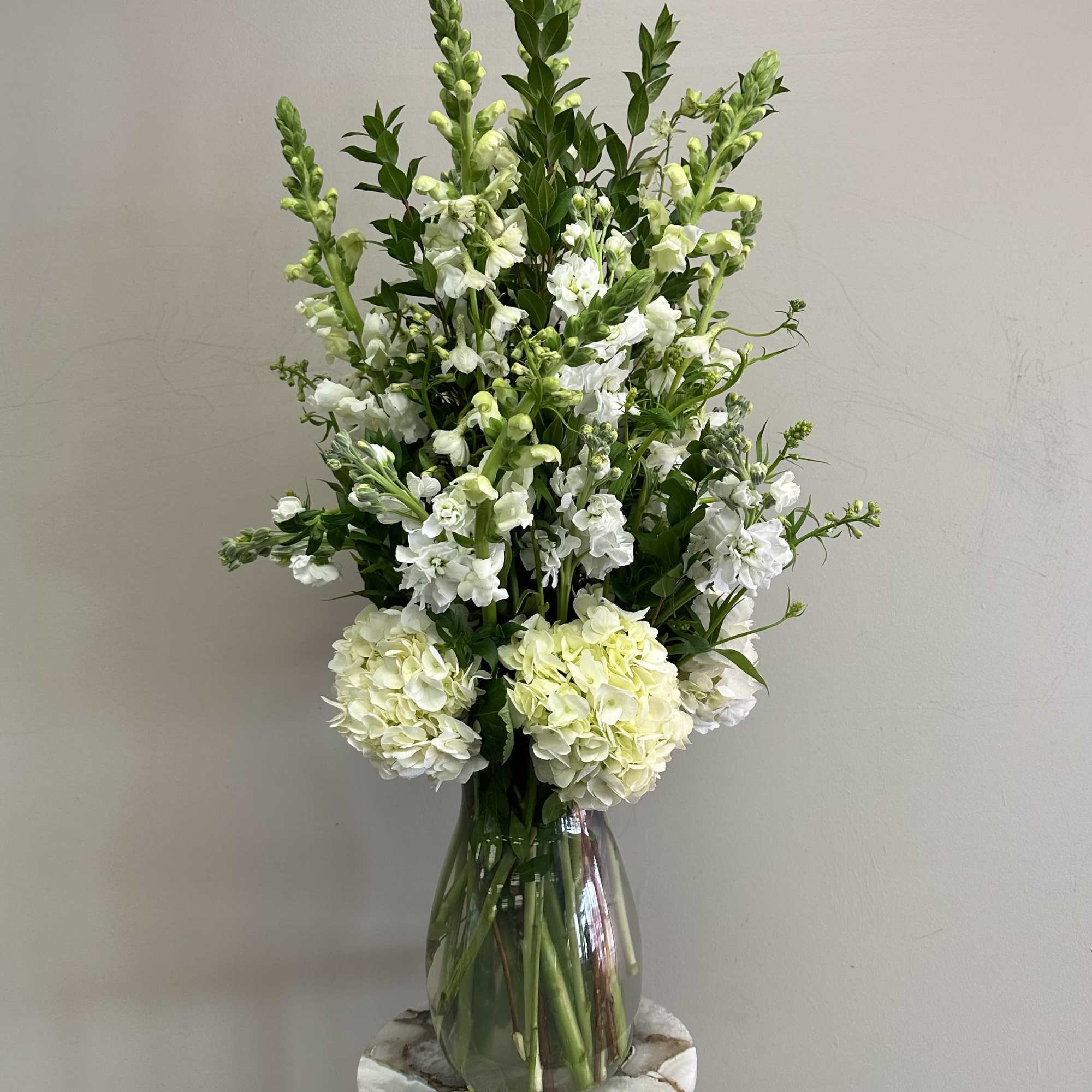 Tall white snapdragons and hydrangeas arranged in a clear glass vase