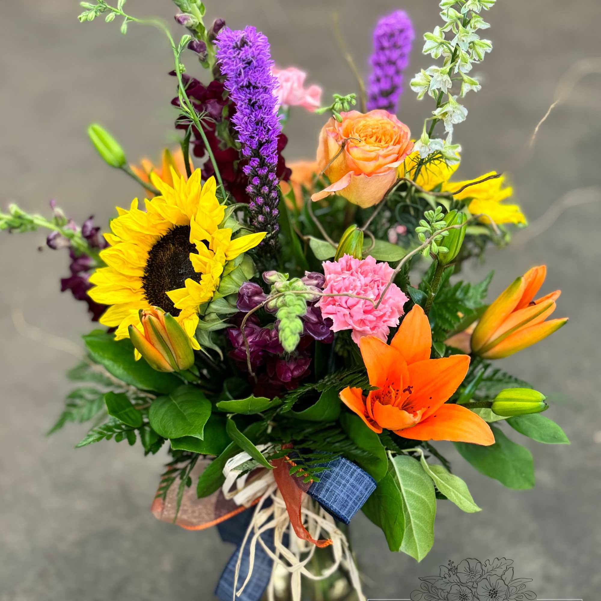 Colorful mixed bouquet with sunflower, lilies, roses, and snapdragons in a glass vase
