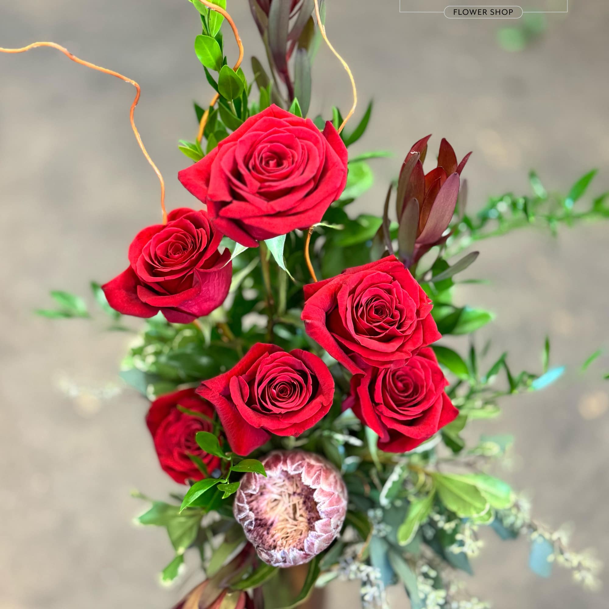 Bouquet of red roses with mixed greenery and protea accents
