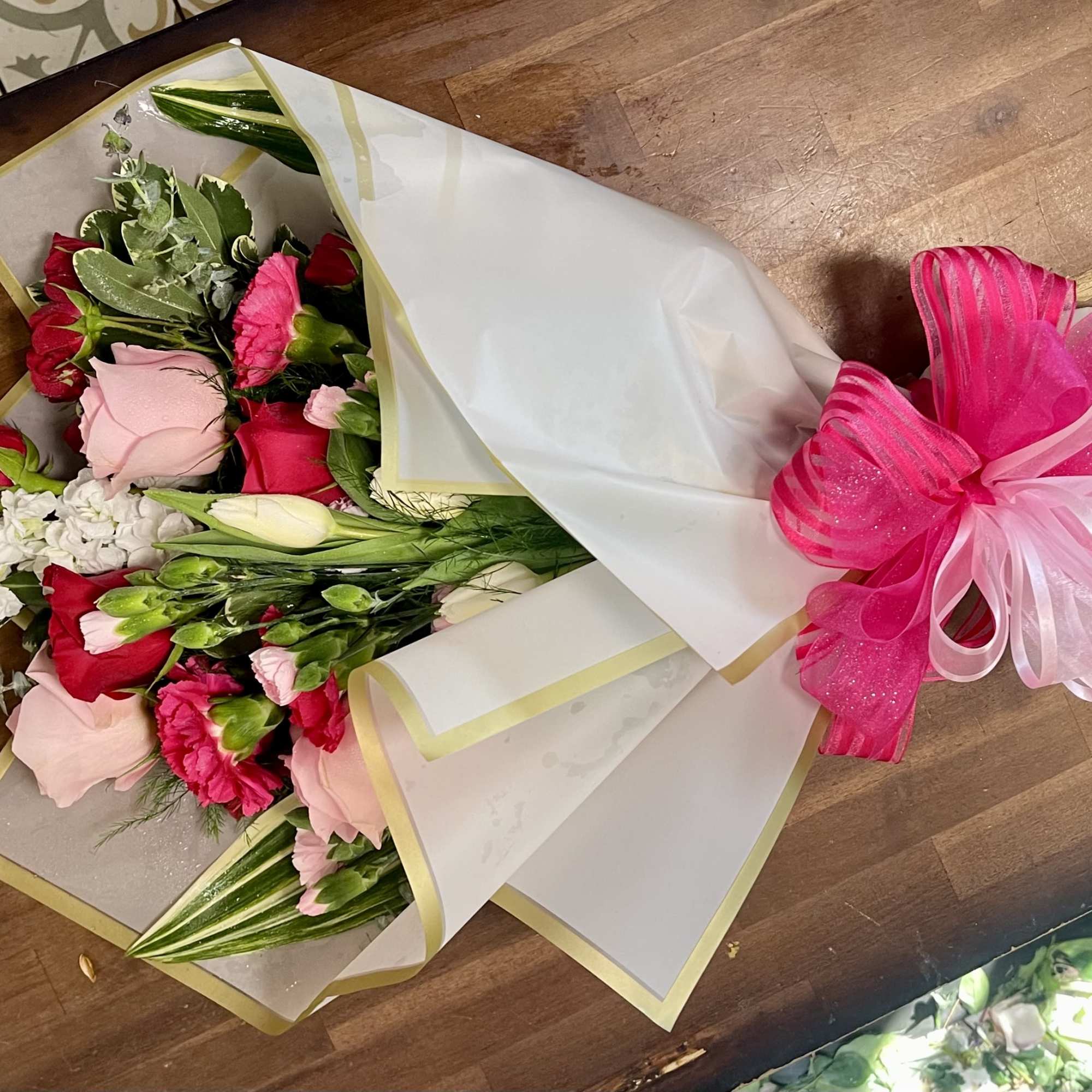Bouquet of red and pink roses wrapped in white paper with a pink ribbon