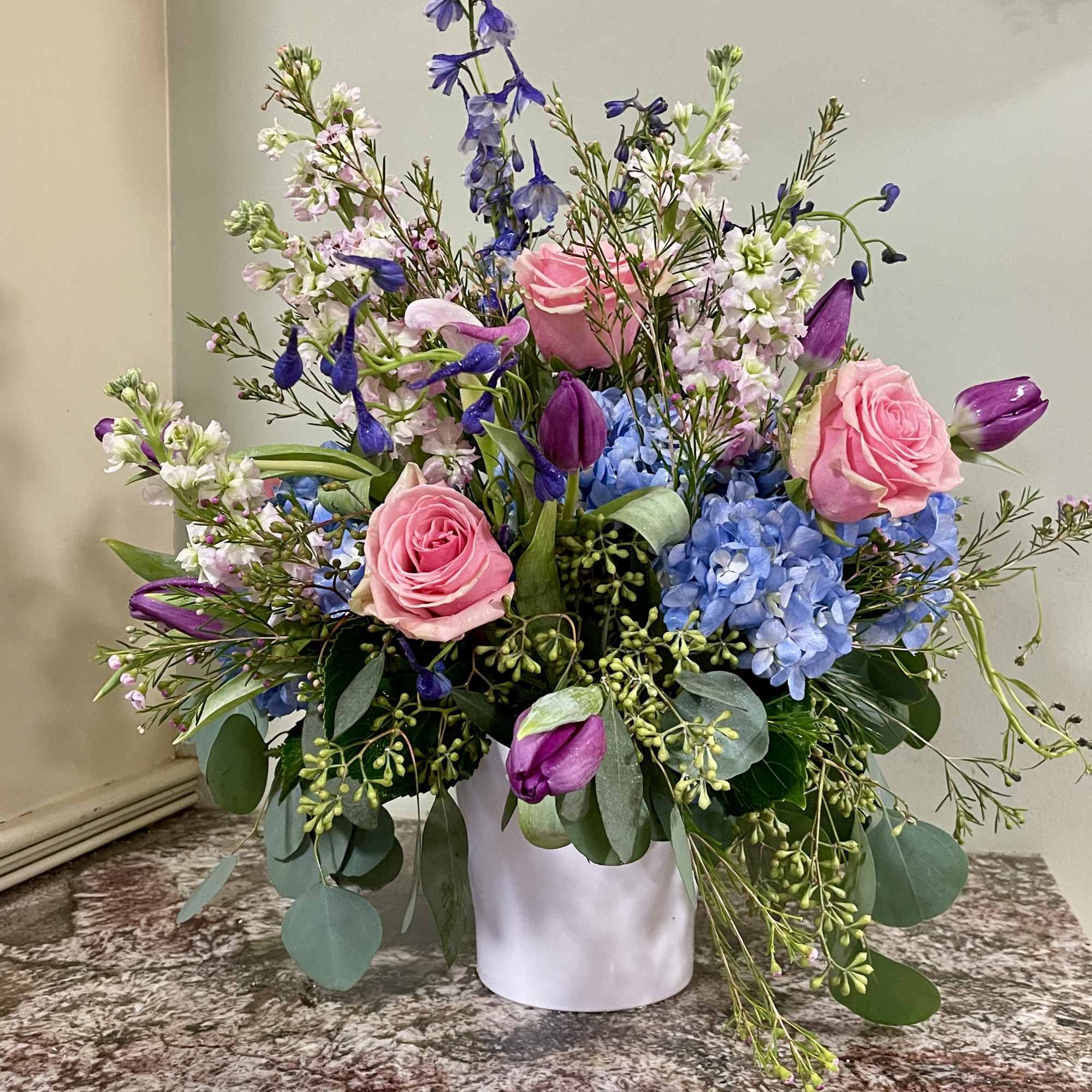 Pink roses, blue hydrangeas, and purple tulips in a white vase