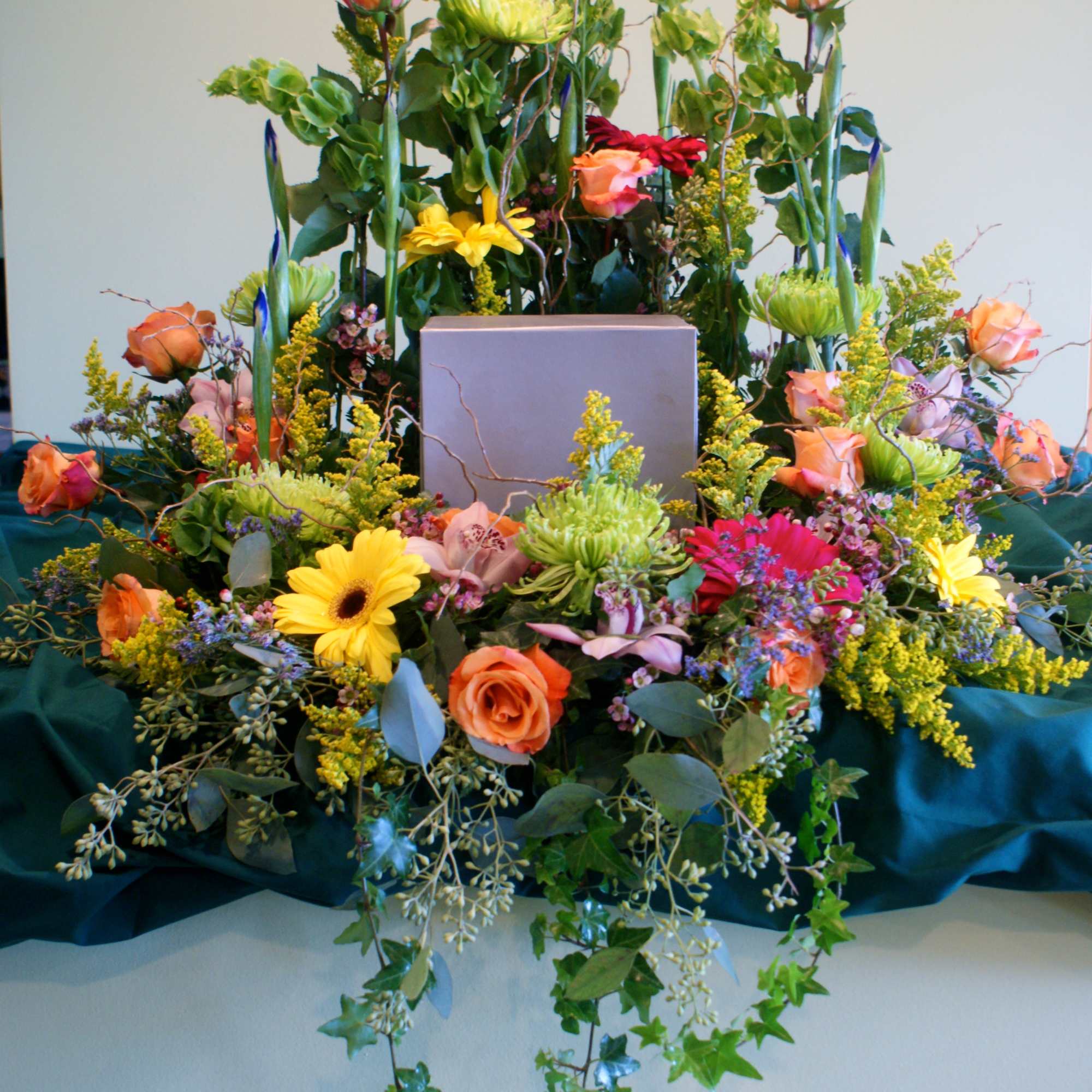 Large floral arrangement with roses, daisies, and mixed blooms around a central box