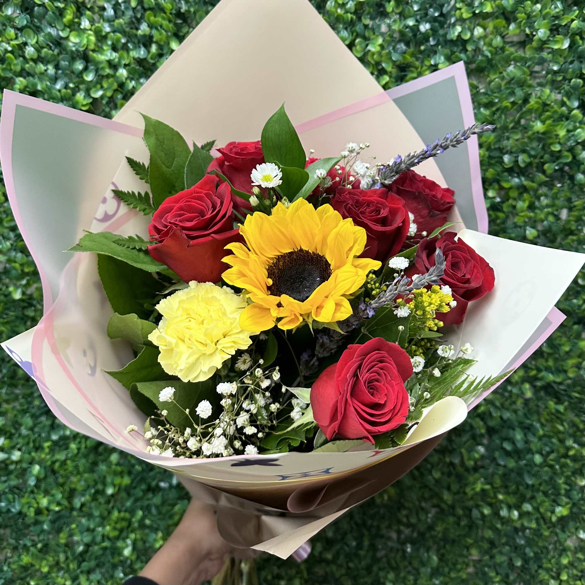 Bouquet of red roses, a sunflower, and yellow carnation in pastel wrap