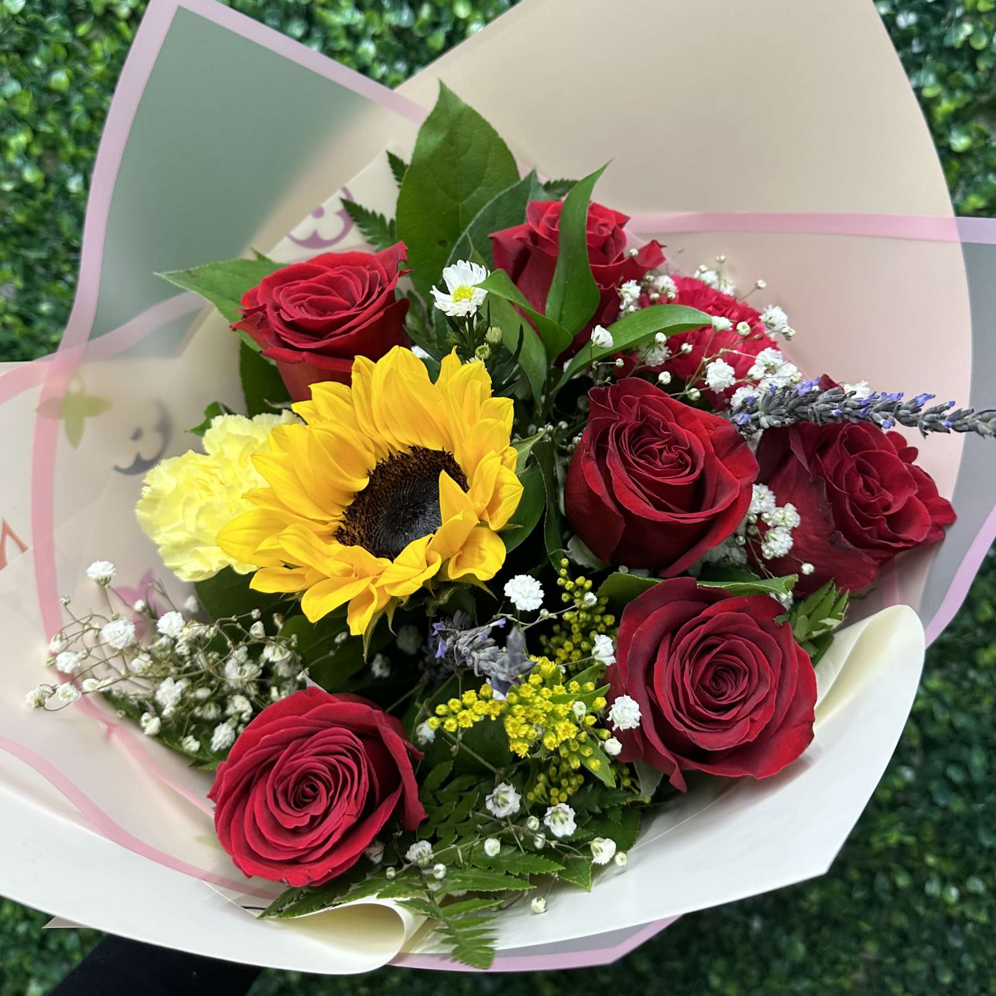 A mixture of red roses with a sunflower and mix filler. Wrapped