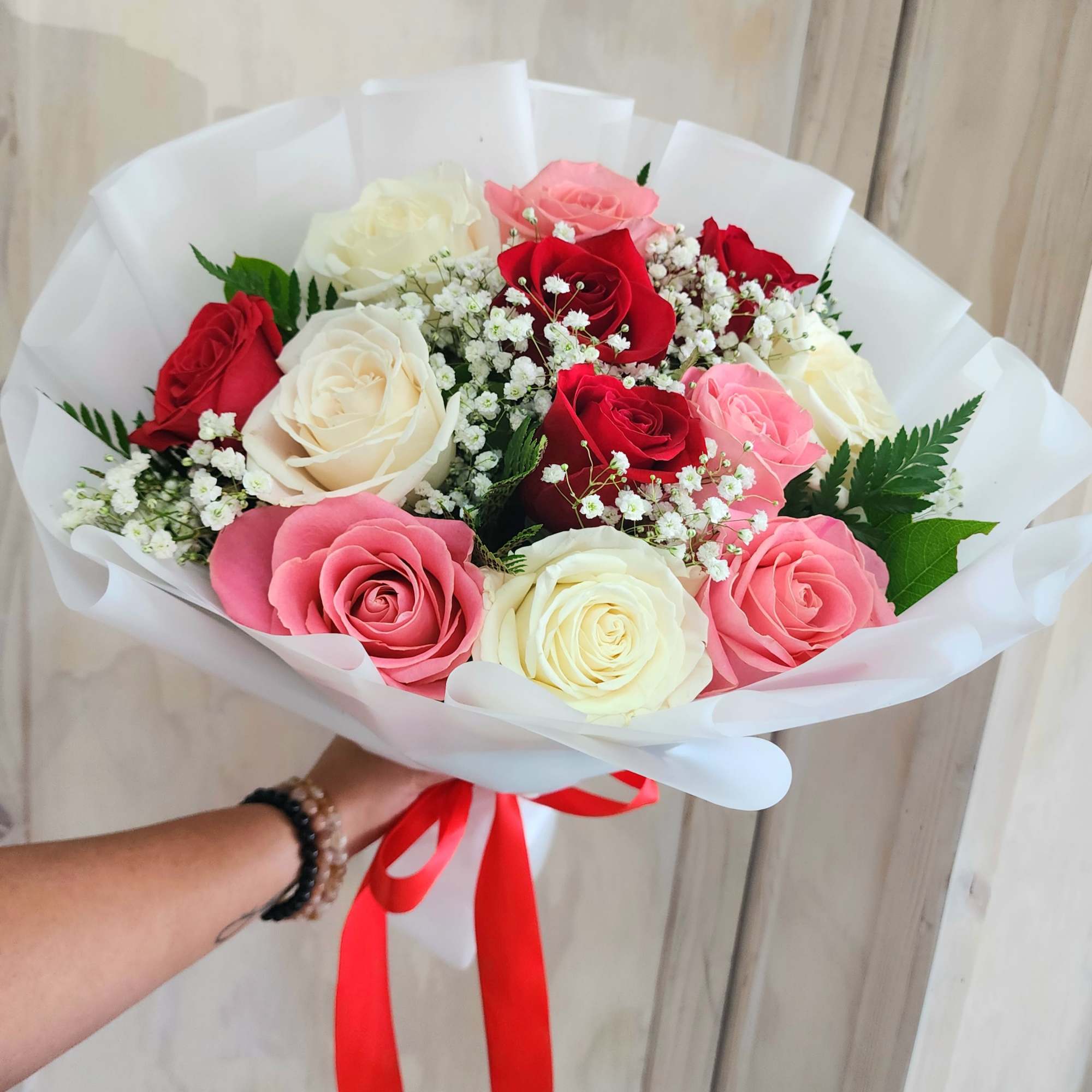 Handheld bouquet of red, pink, and white roses with baby's breath
