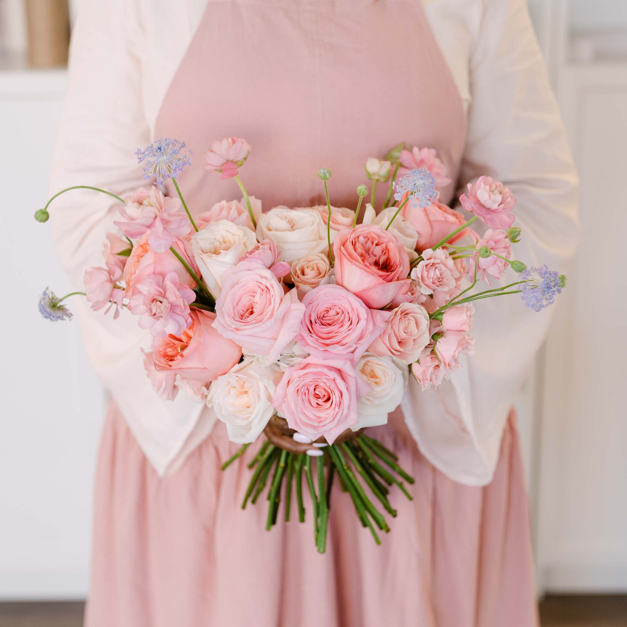 Person holding a bouquet of pink and white roses with small blue flowers