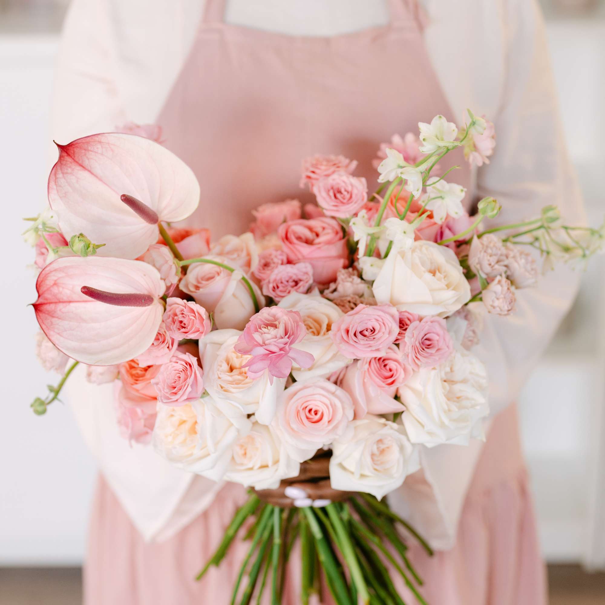 Pink and white bouquet with roses and anthuriums held by a person in an apron