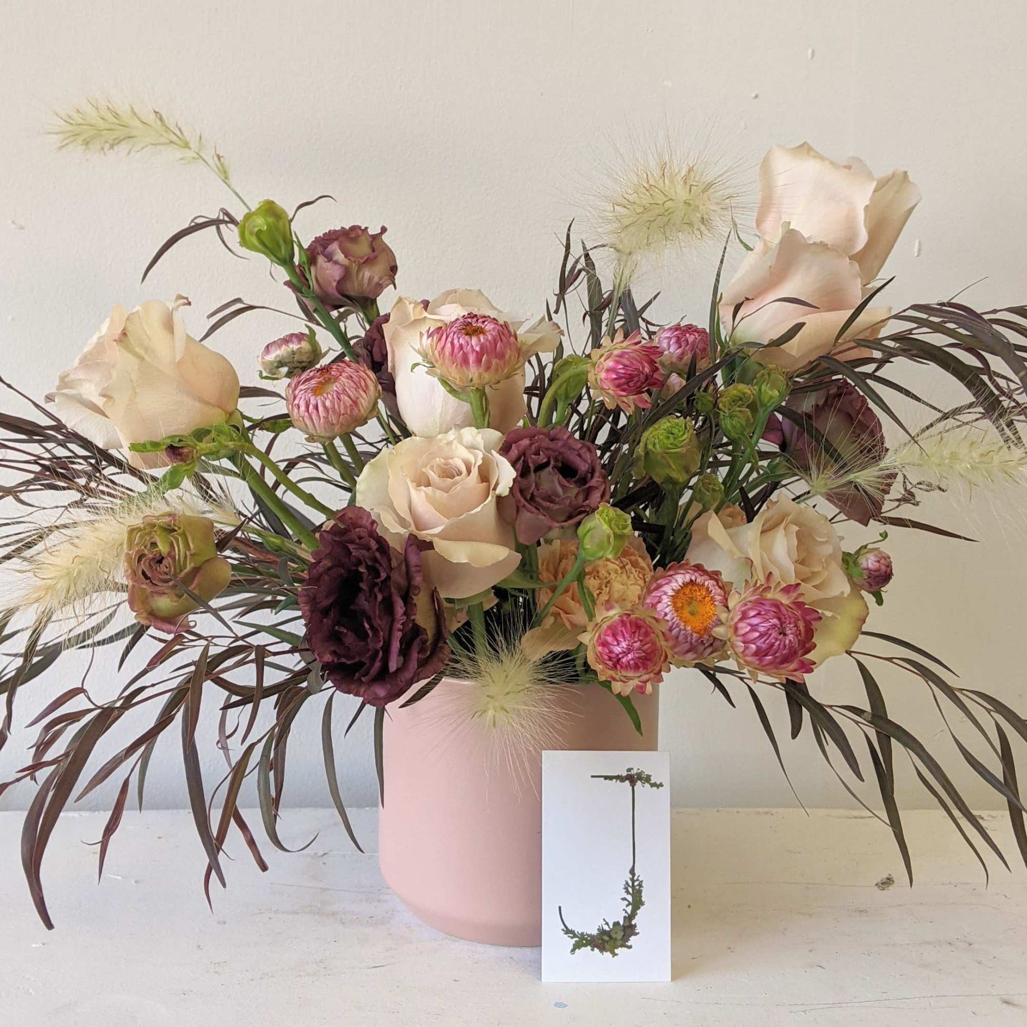 Mixed bouquet of blush and burgundy flowers in a pink vase