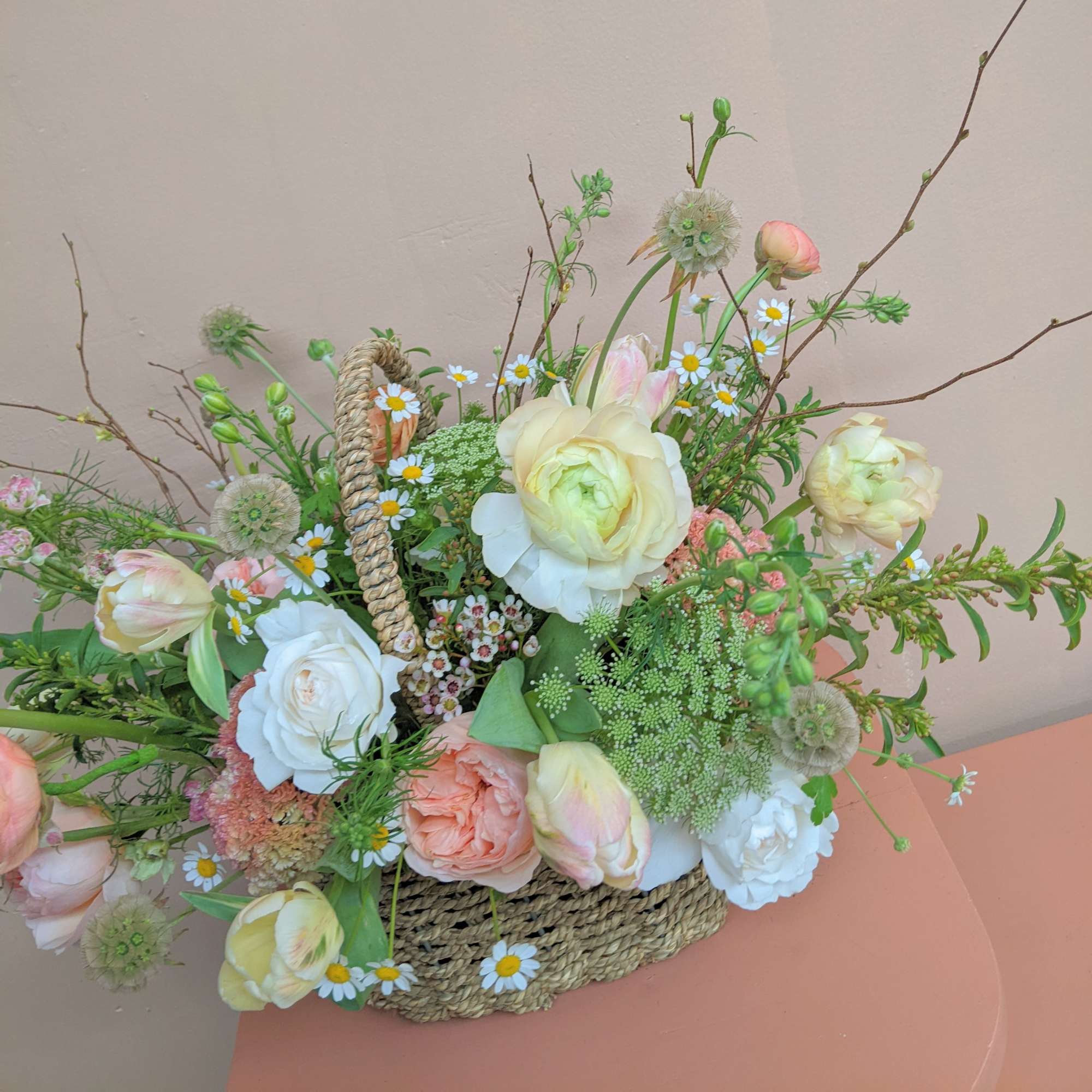 Pastel flower arrangement in a woven basket with roses, tulips, and daisies