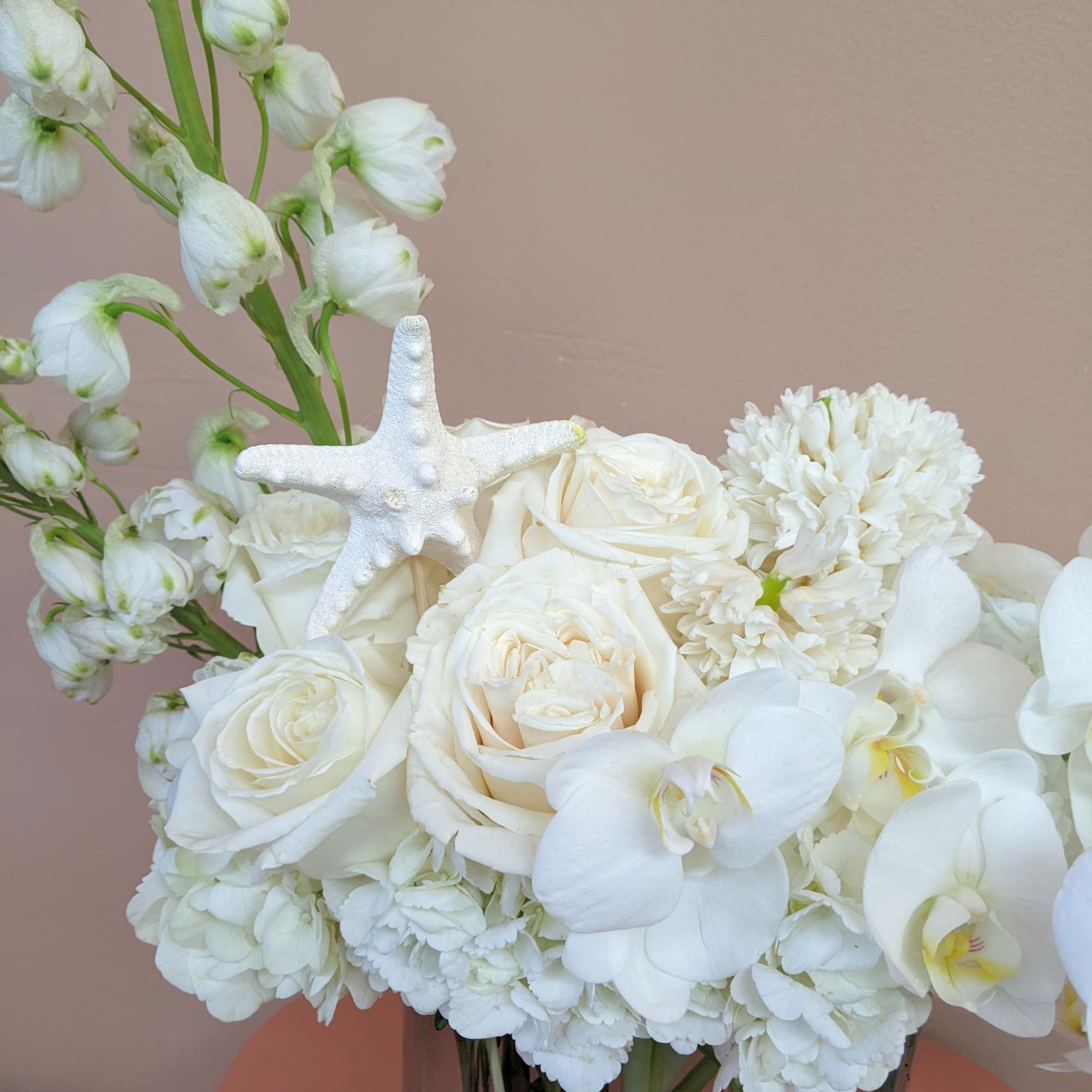 White floral arrangement with roses, orchids, and a starfish accent in a vase
