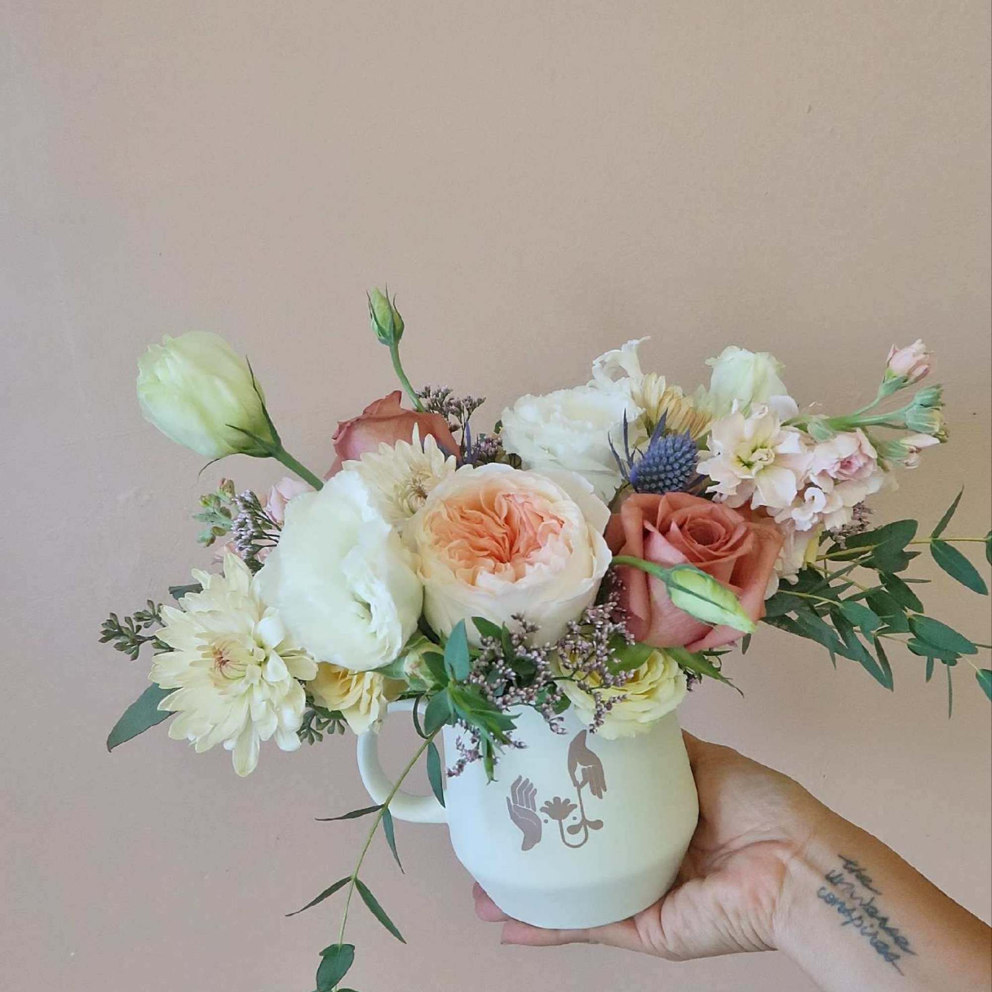 Mixed bouquet of pastel roses and white blooms in a white mug