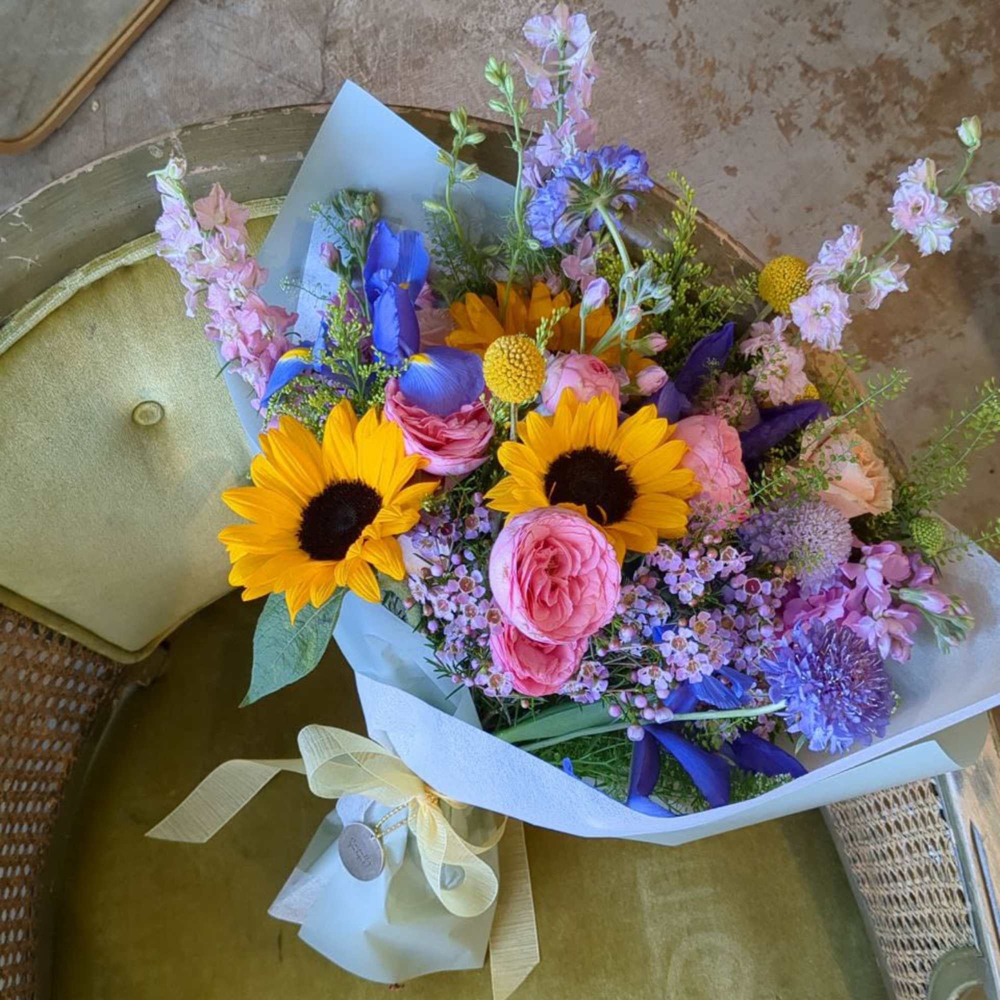 Bouquet of sunflowers, pink roses, and purple flowers wrapped in pale paper