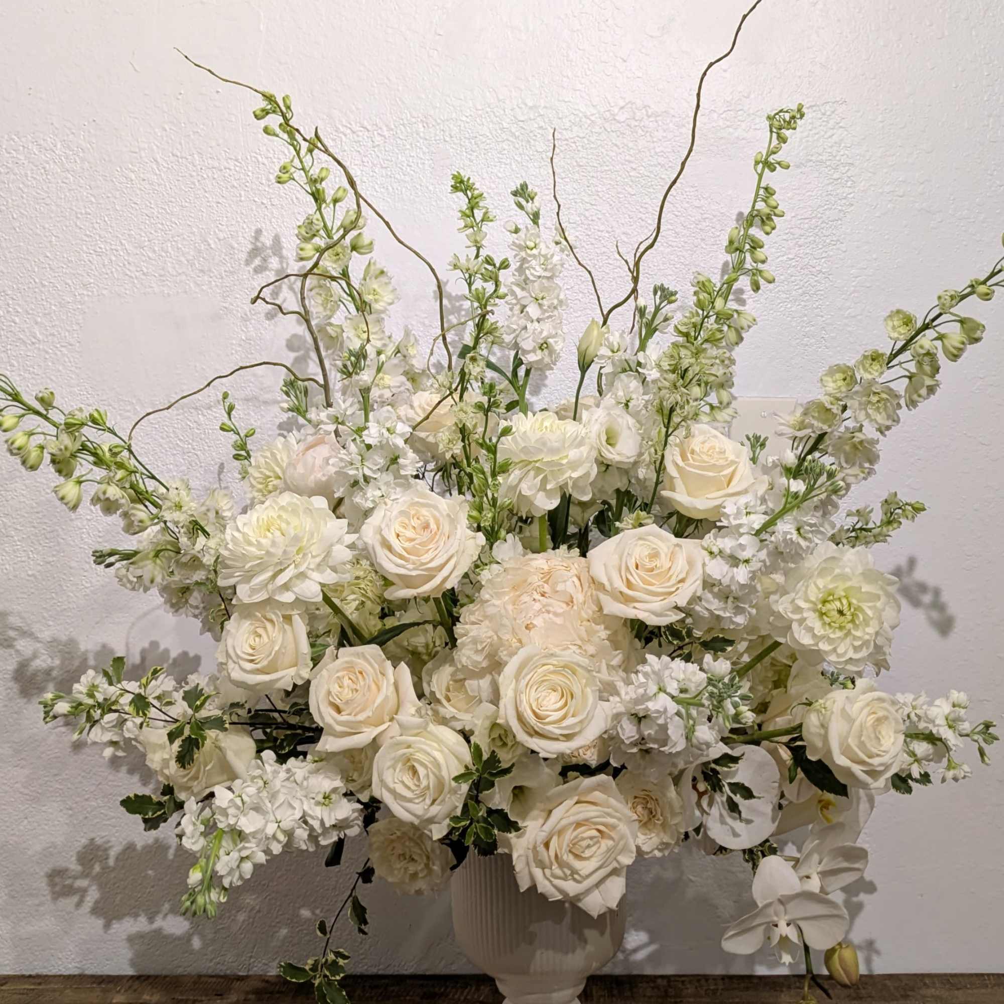Large white floral arrangement in a pedestal vase with roses and orchids