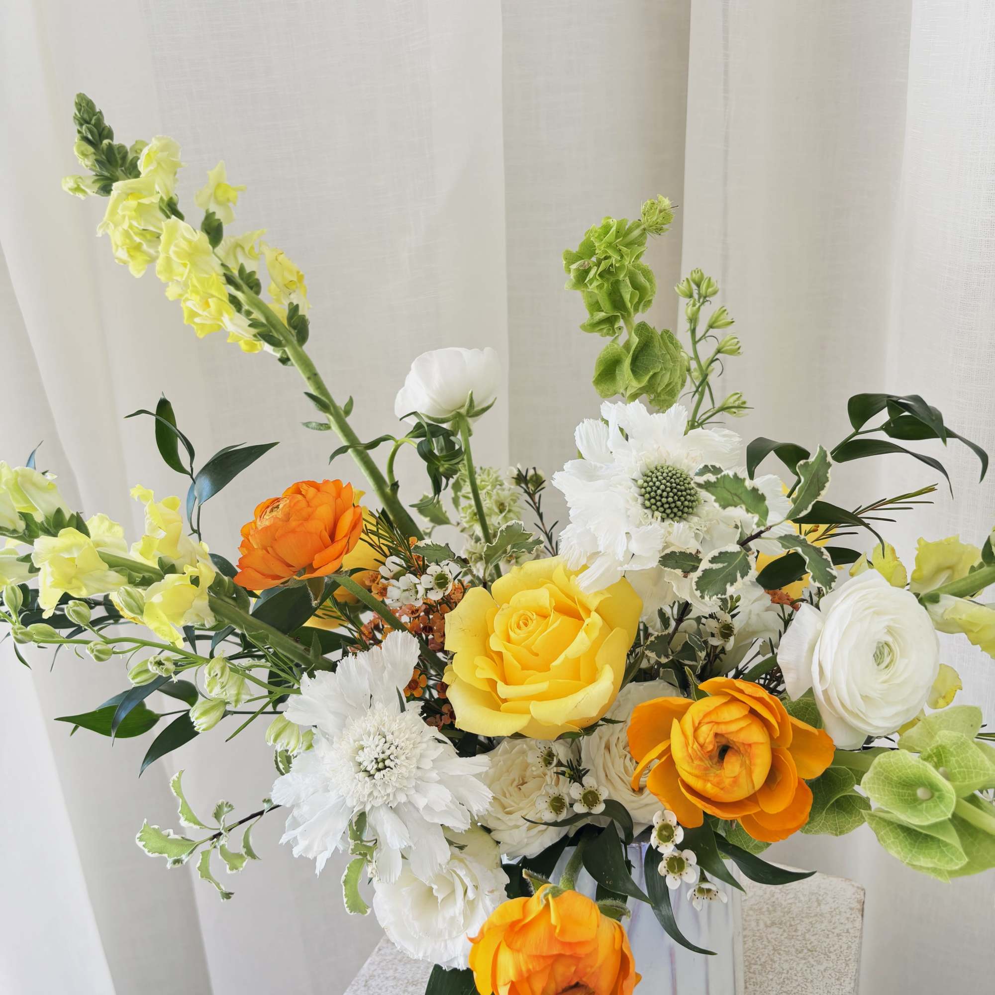 Bright mixed flower arrangement in a white vase with yellow, orange, and white blooms