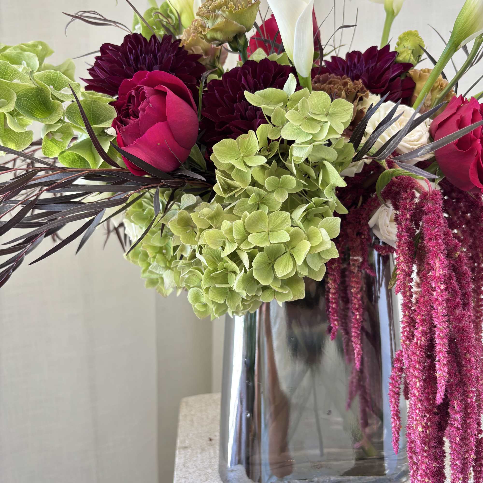 Bouquet of white calla lilies, burgundy blooms, and green hydrangeas in a glass vase