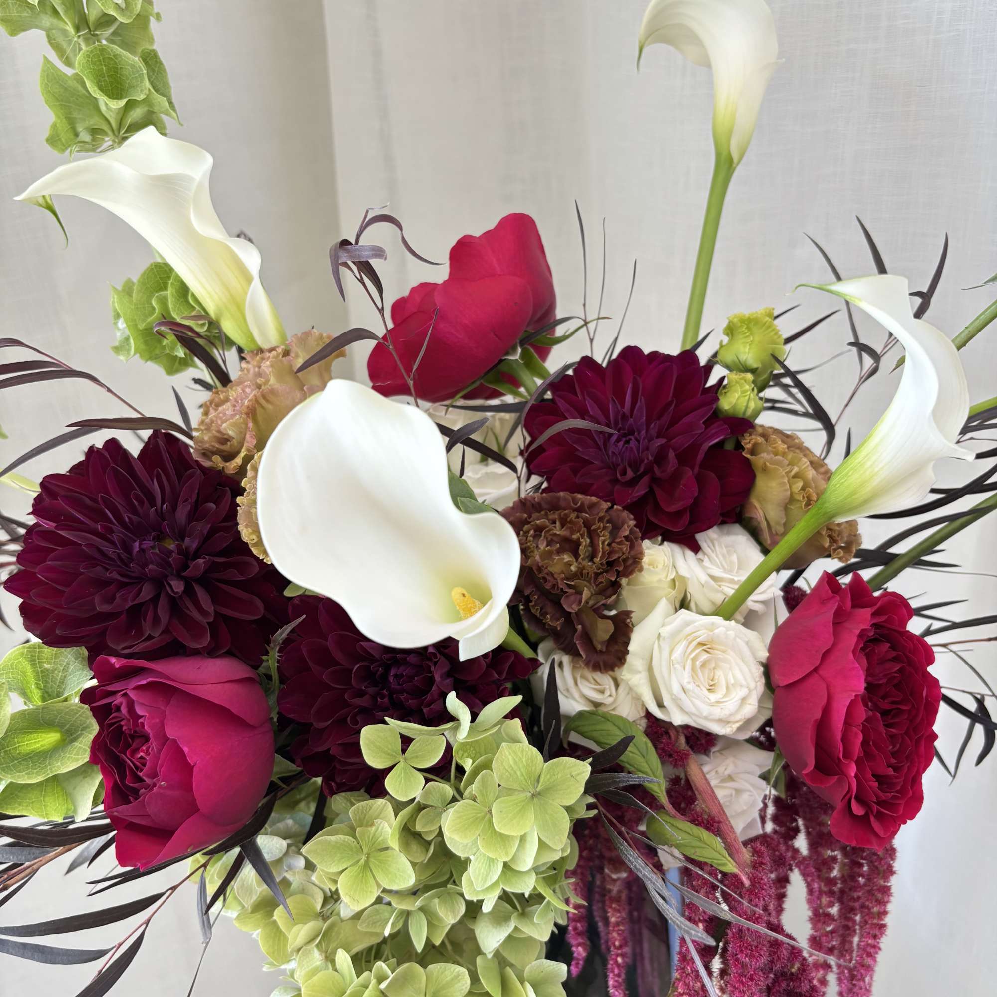 Bouquet of white calla lilies, red roses, and dark burgundy dahlias in a vase