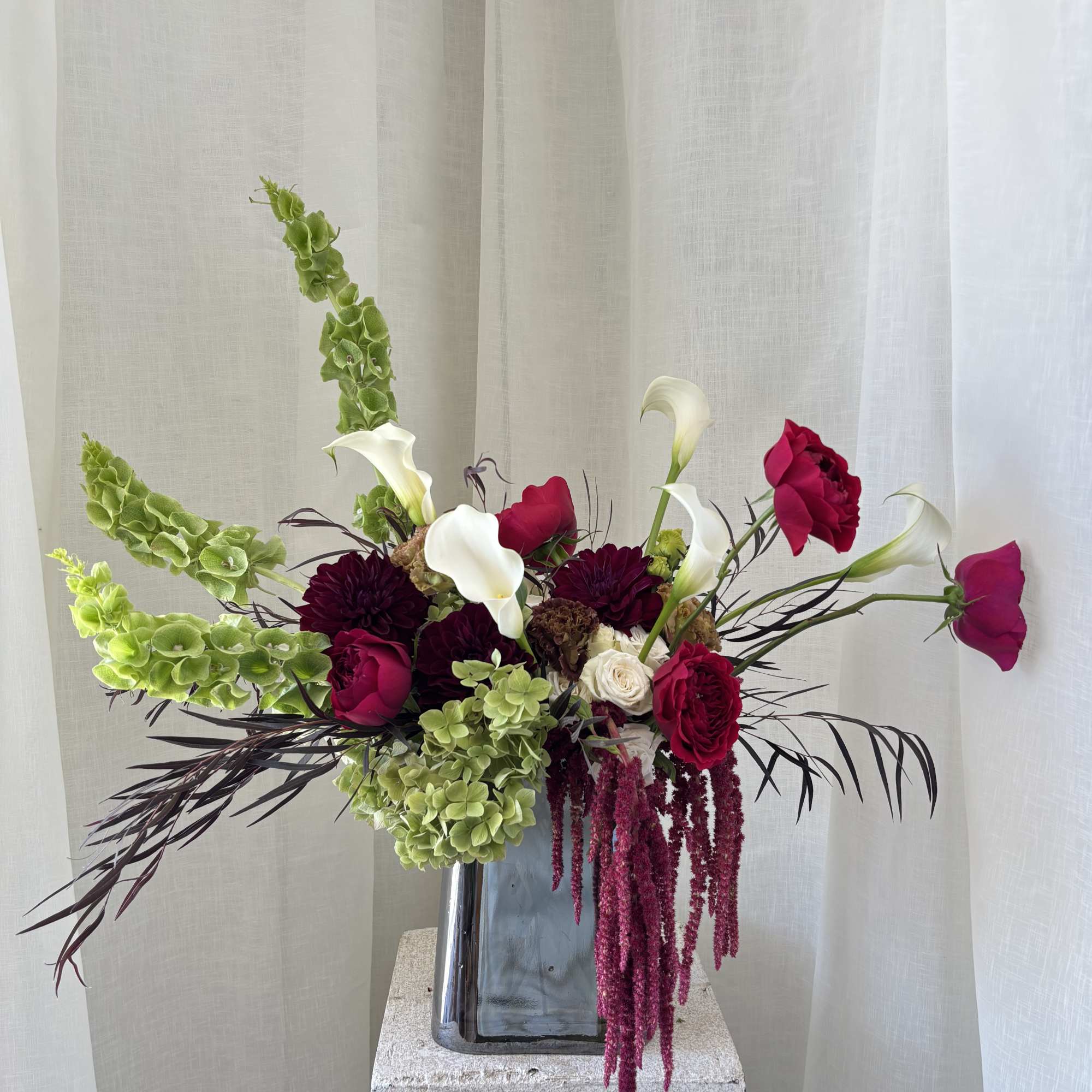 Tall floral arrangement with white calla lilies, magenta roses, and green hanging blooms in a vase.