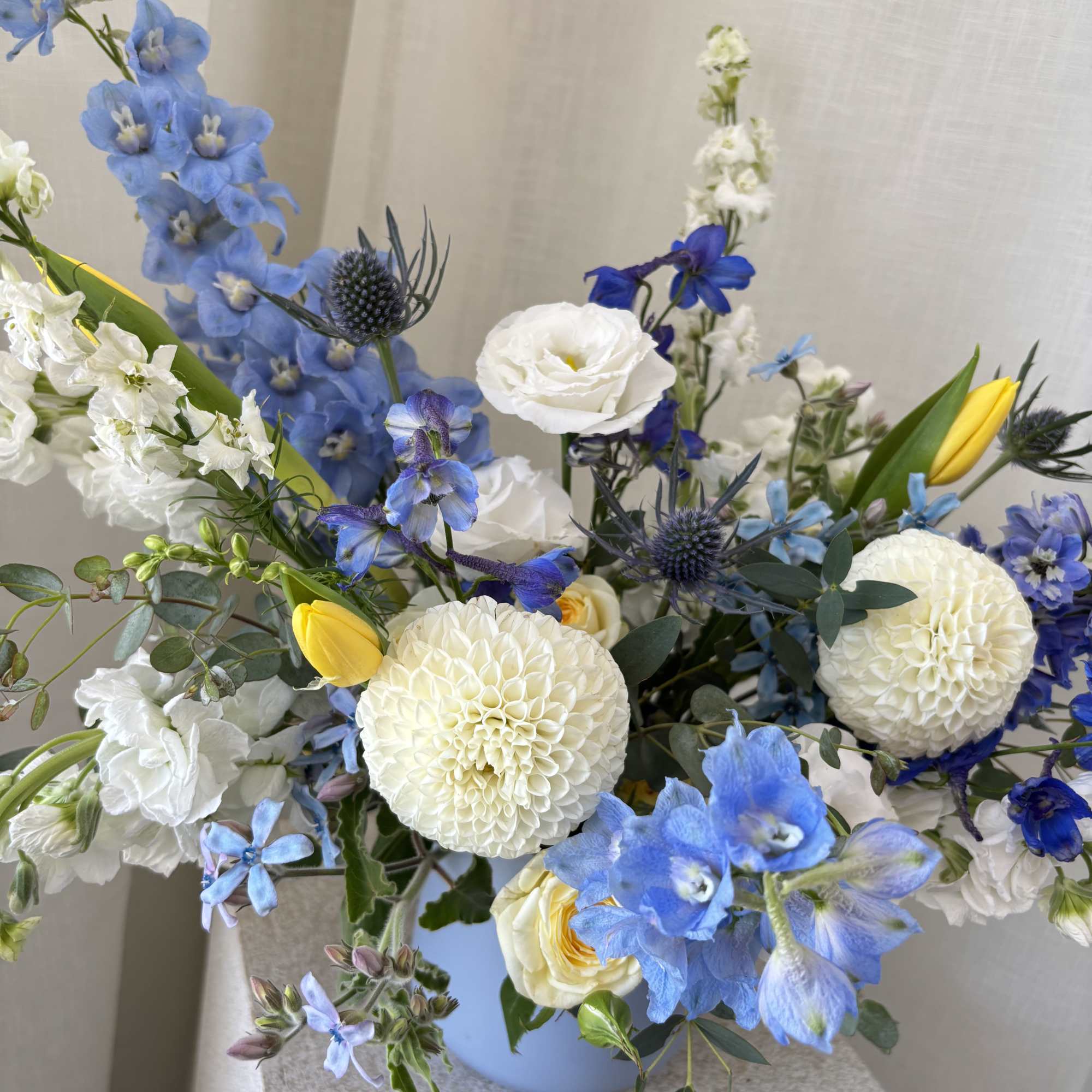 Blue and white mixed flower arrangement in a light blue vase