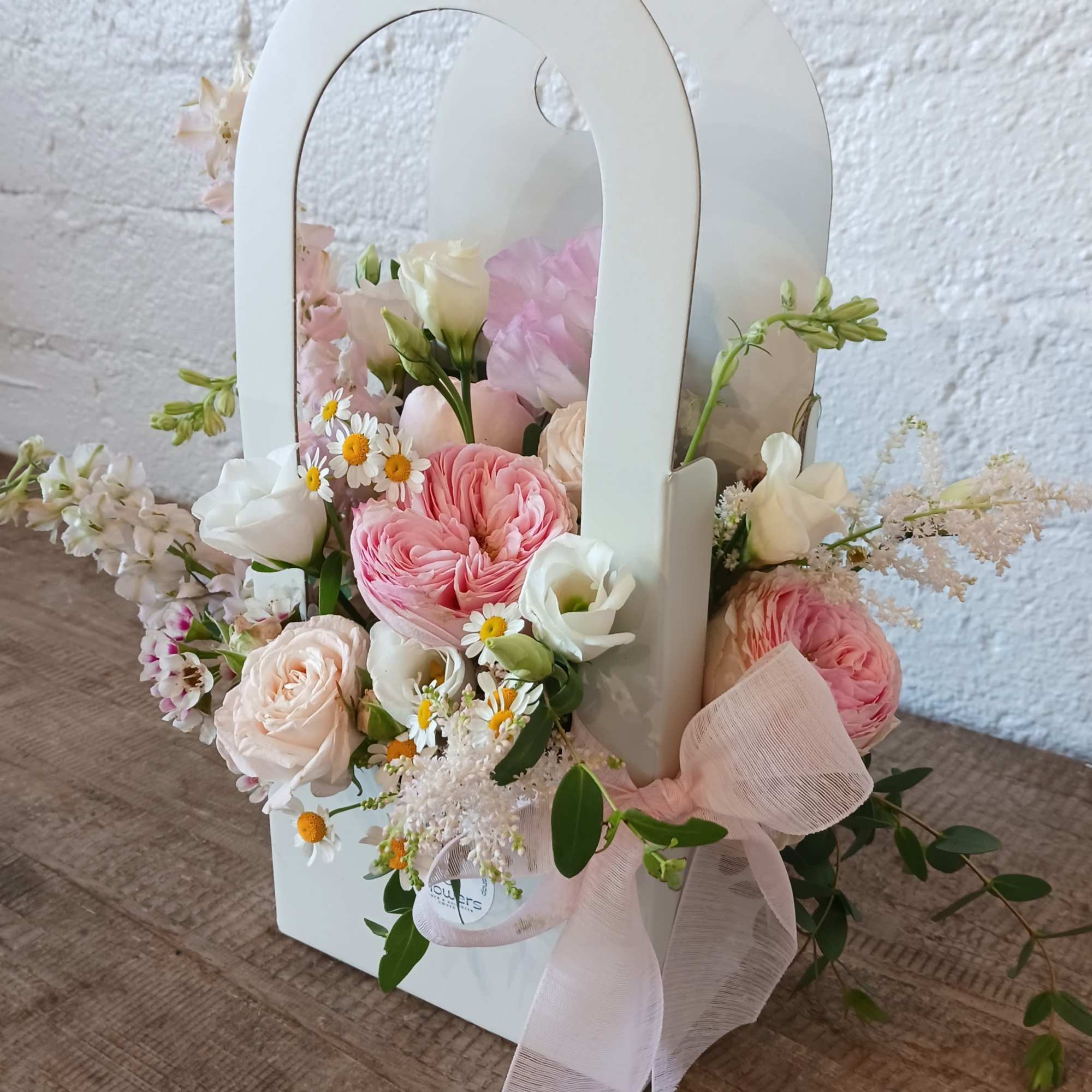 Pink and white flowers arranged in a white handled gift box with a ribbon