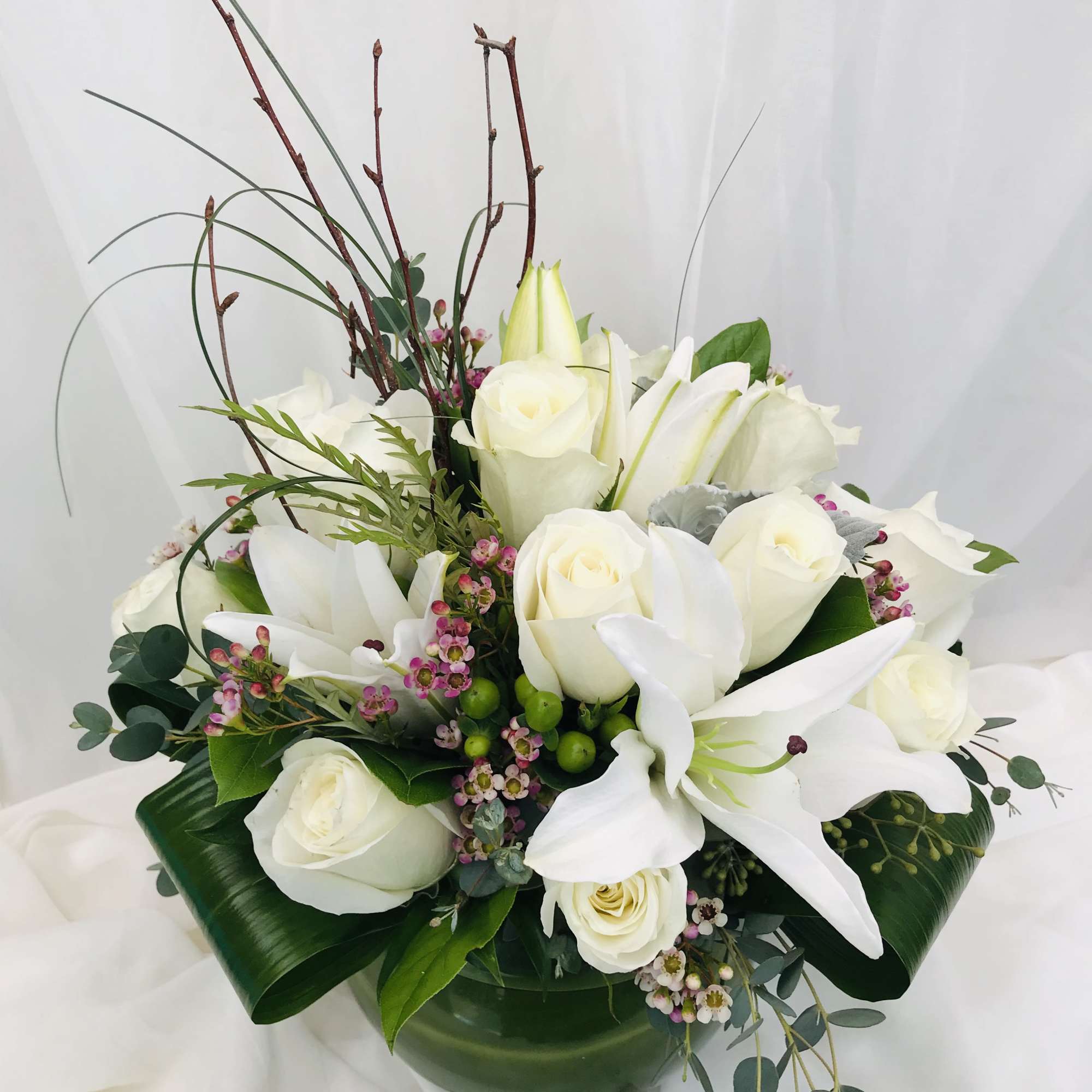 White roses and lilies arranged in a low vase with greenery