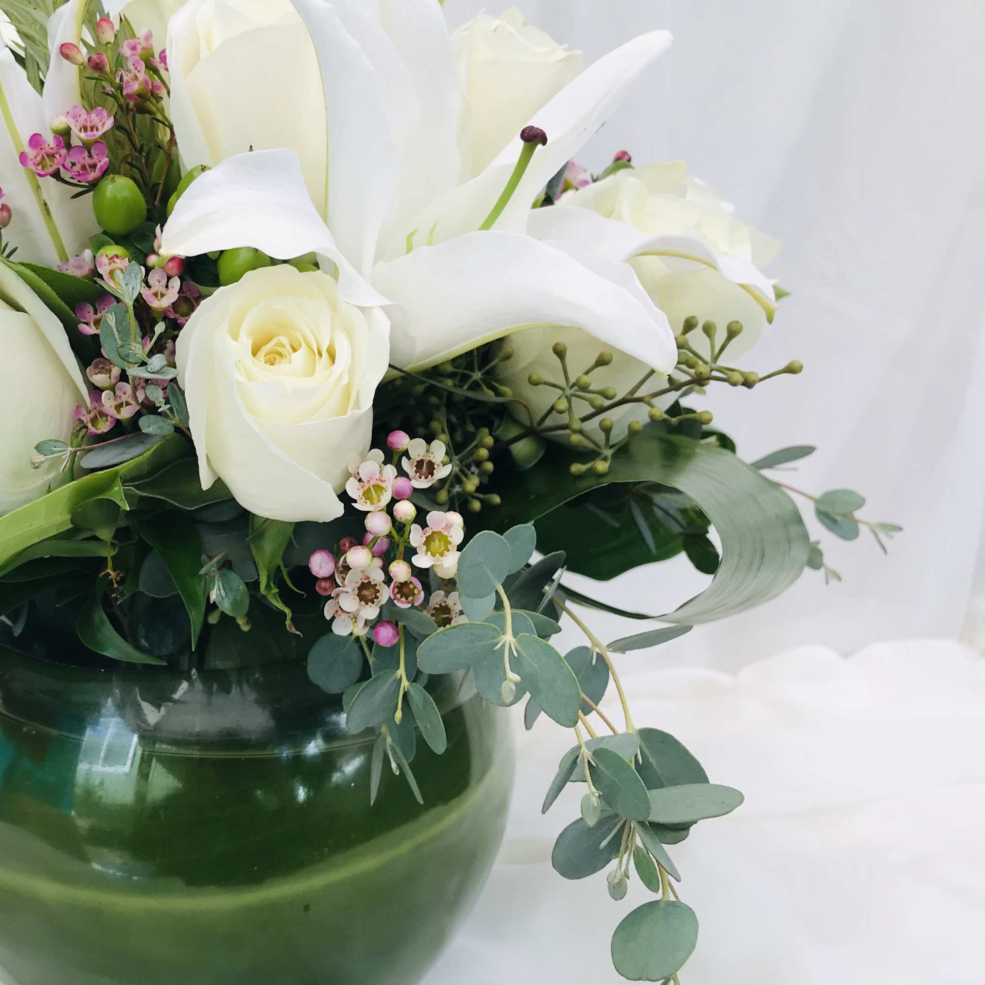 White roses and calla lilies in a green glass vase with pink accent flowers