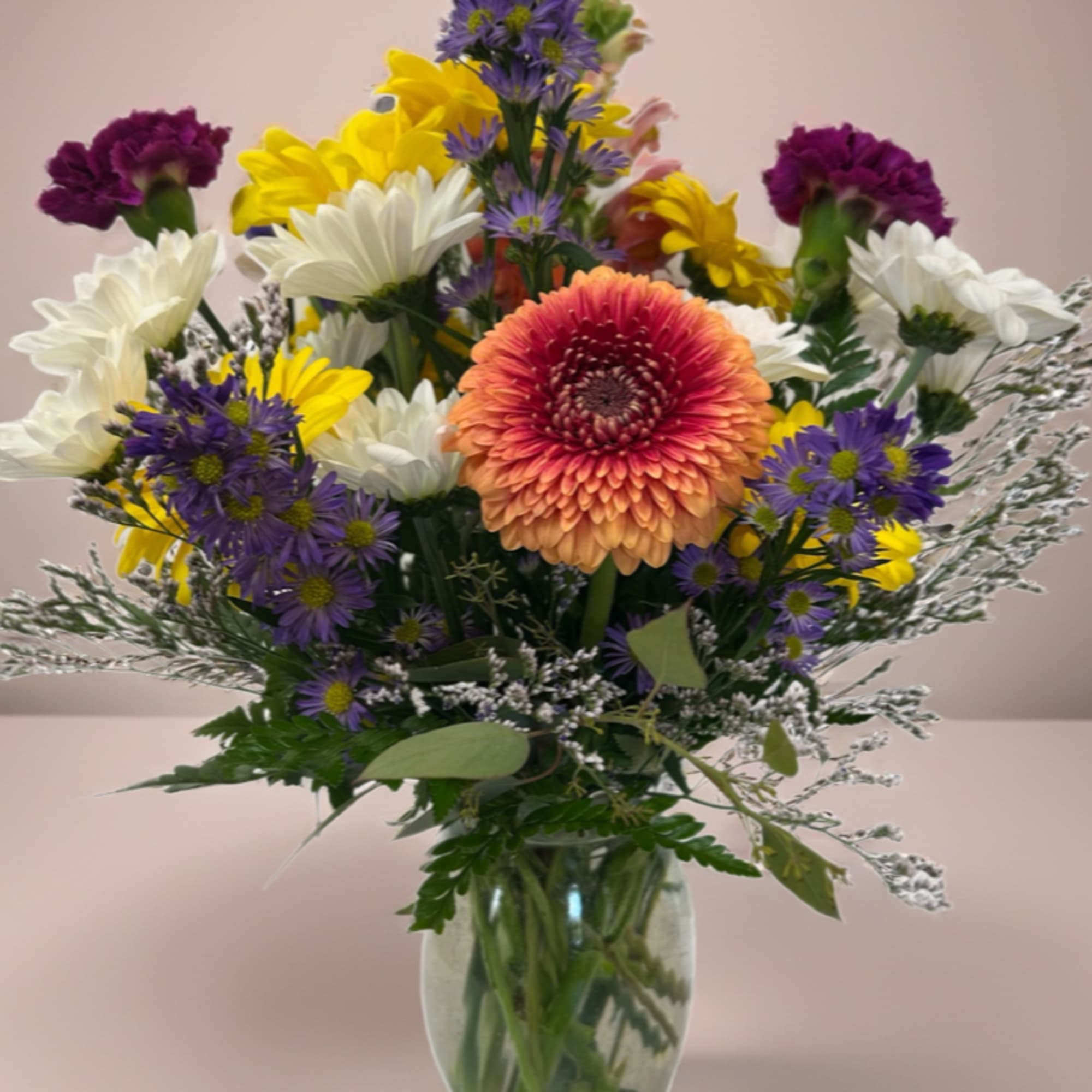 Mixed bouquet in a glass vase with purple, yellow, white, and peach flowers.