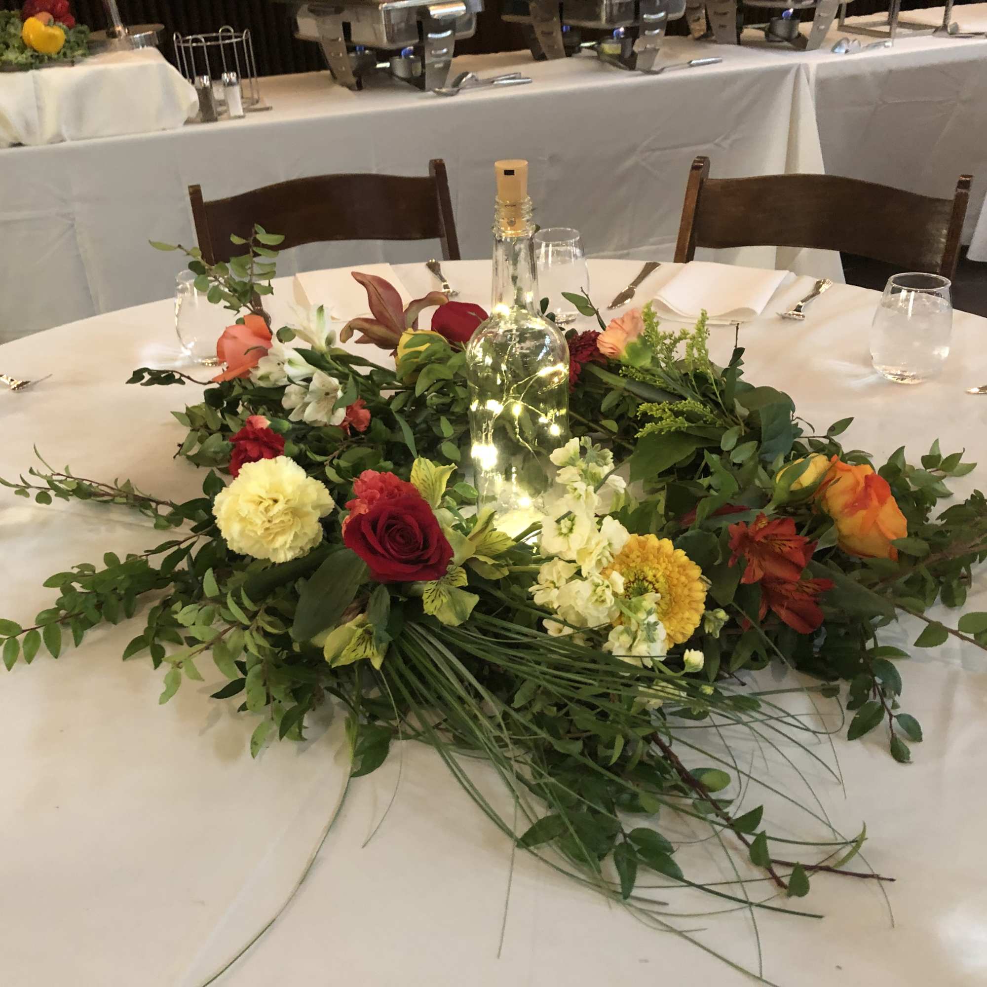 Round table centerpiece with mixed flowers around a bottle and string lights