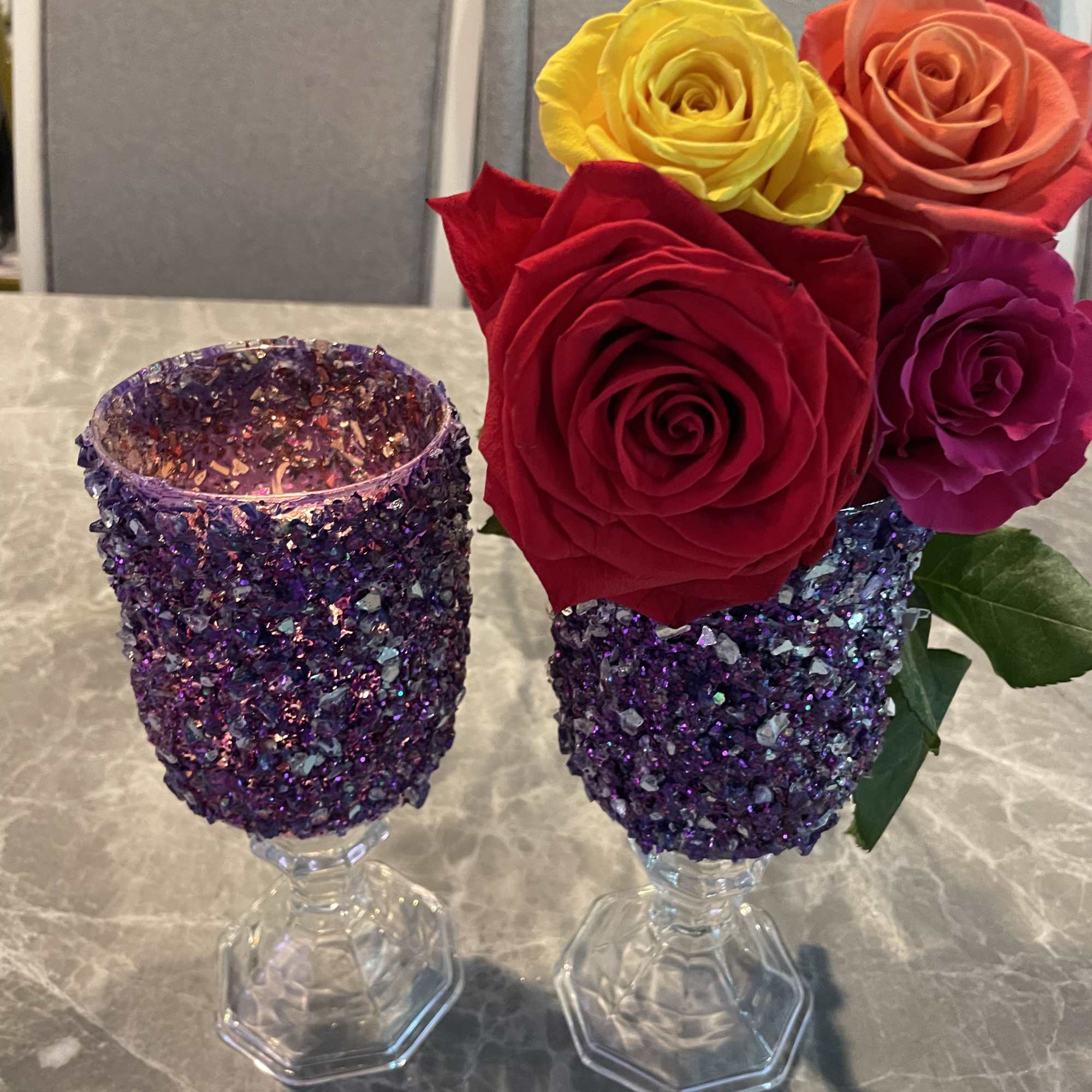 Two glitter-covered goblets hold colorful roses on a table.