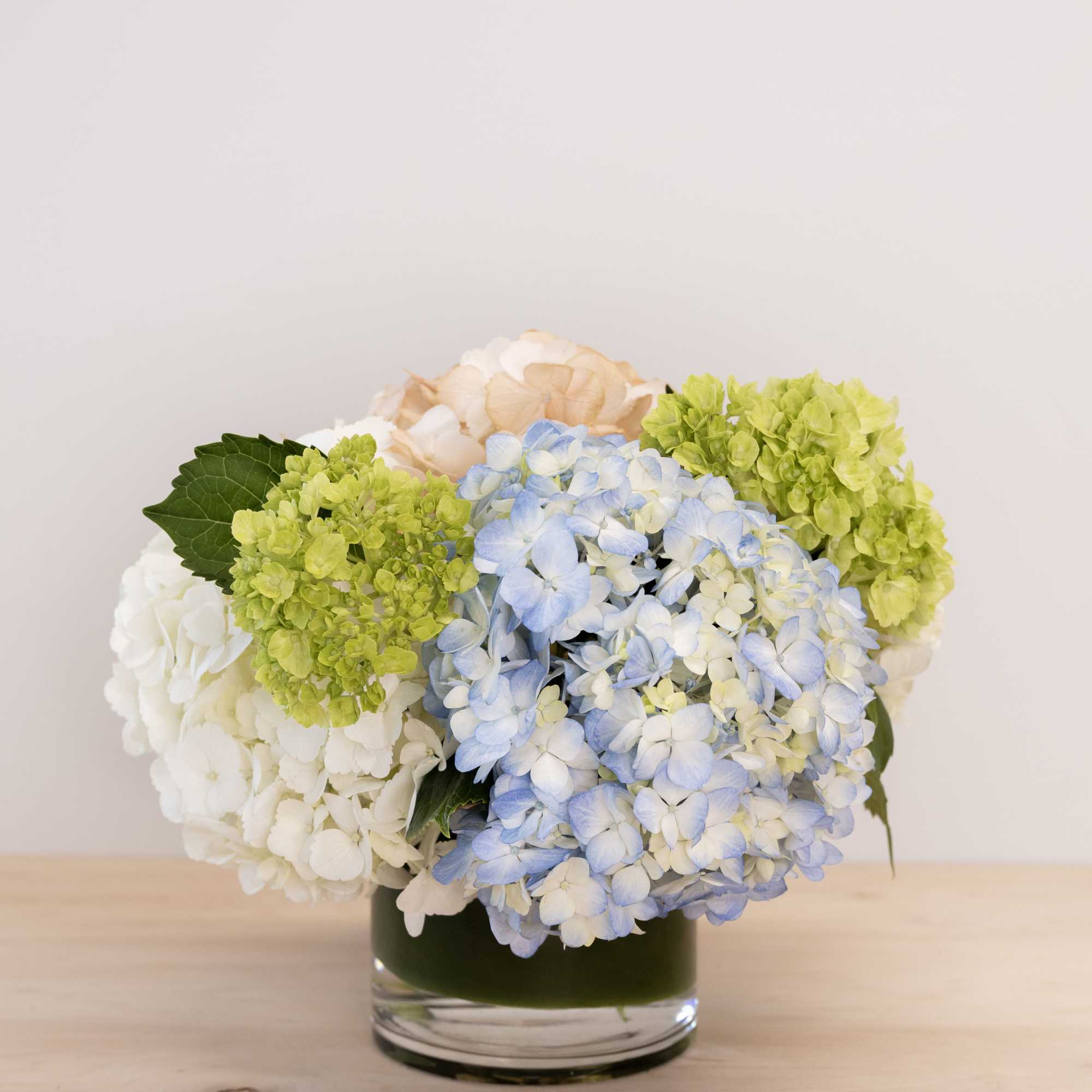 Hydrangea arrangement in a glass vase with blue, white, green, and peach blooms
