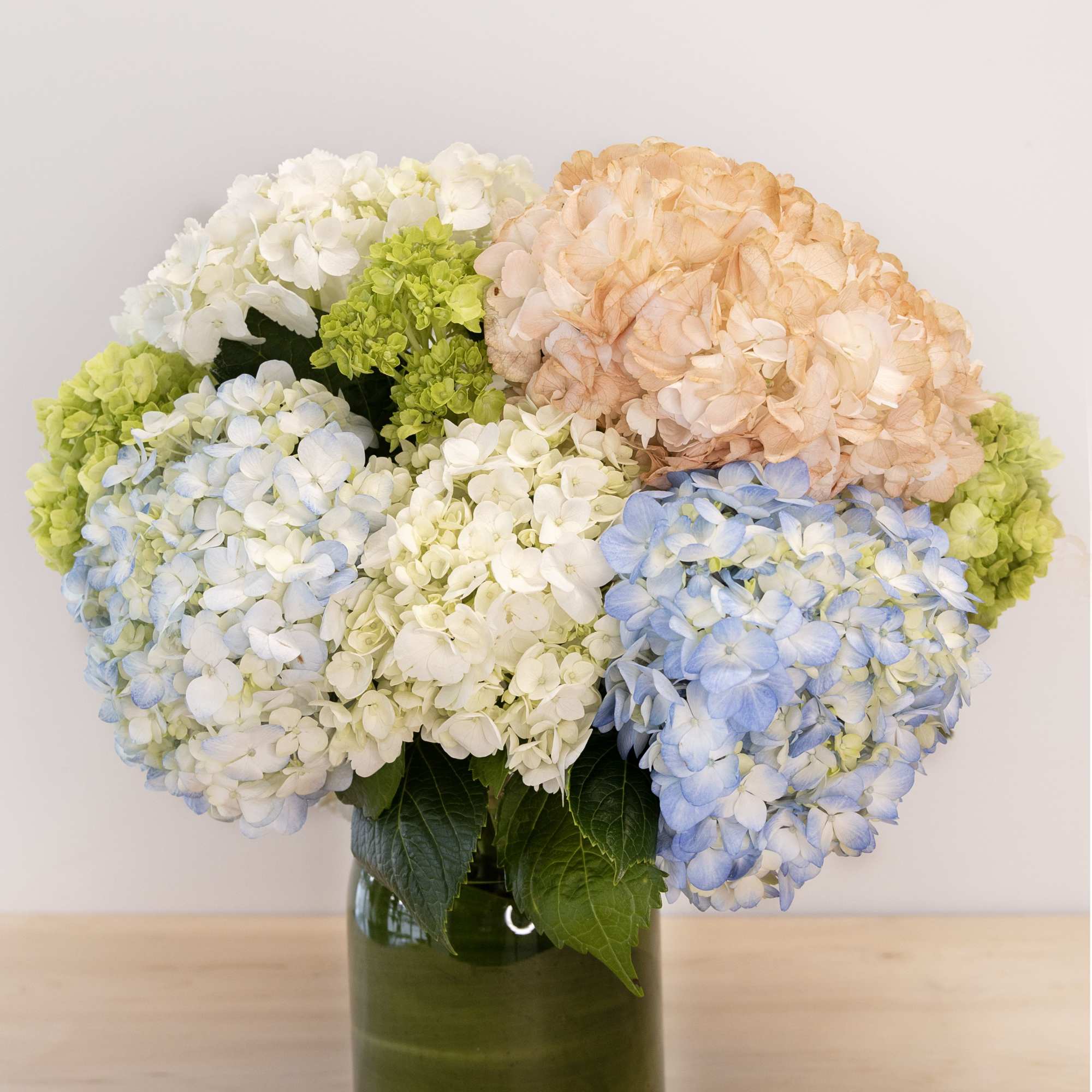 Bouquet of pastel hydrangeas in a green glass vase