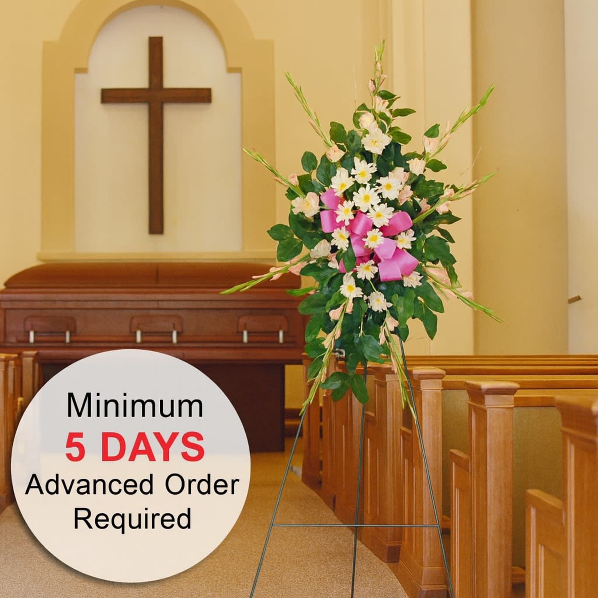 Standing spray of white and pink flowers with a pink bow on an easel in a church