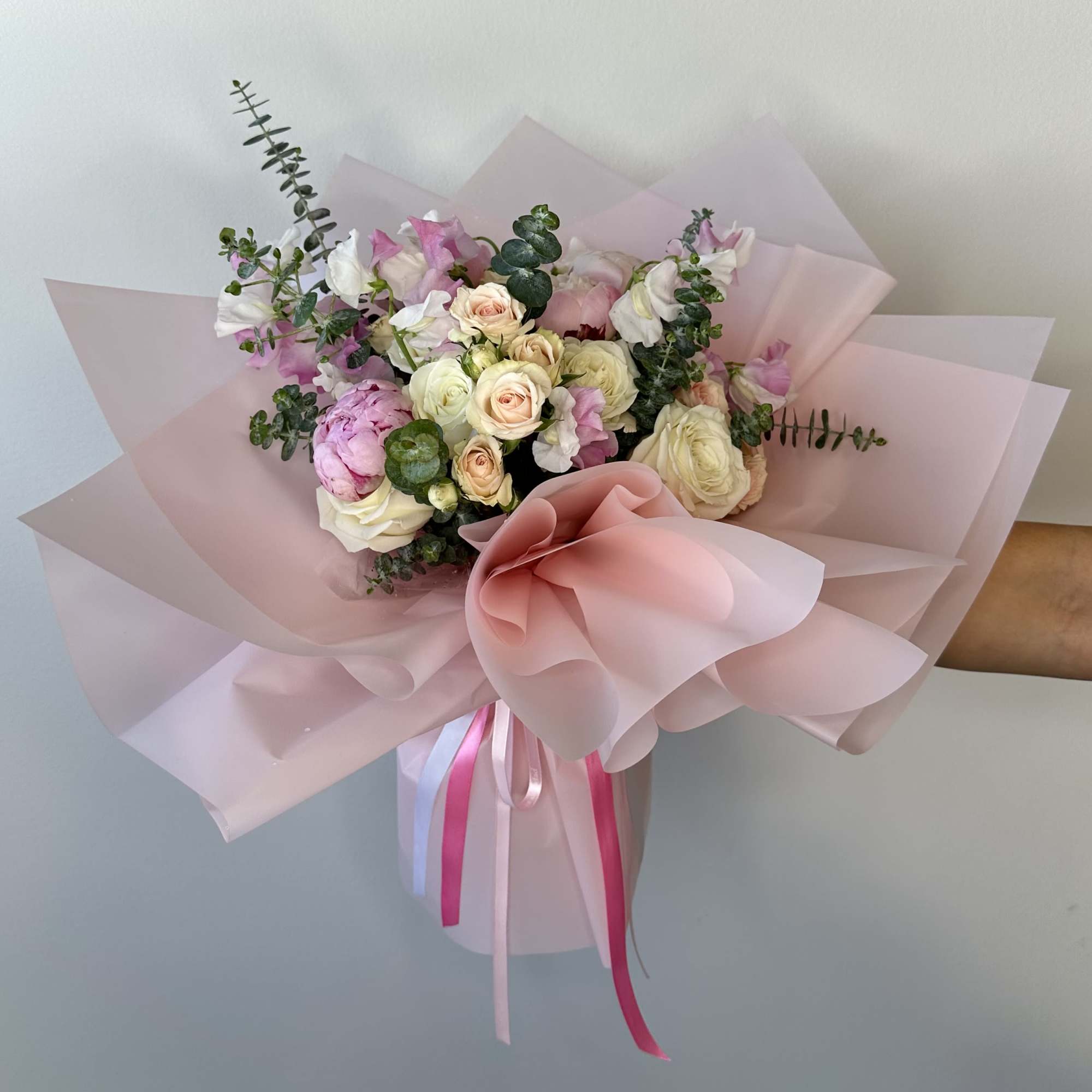 Pink and white bouquet of roses and peonies wrapped in pale pink paper