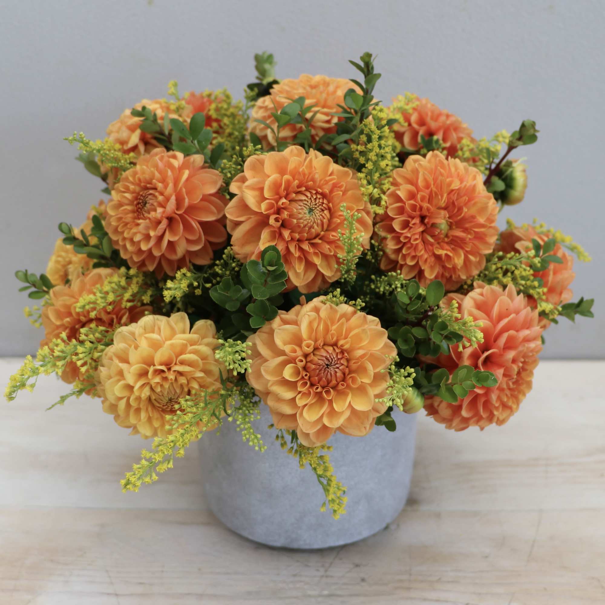 Low arrangement of orange dahlias with yellow accents in a gray ceramic pot