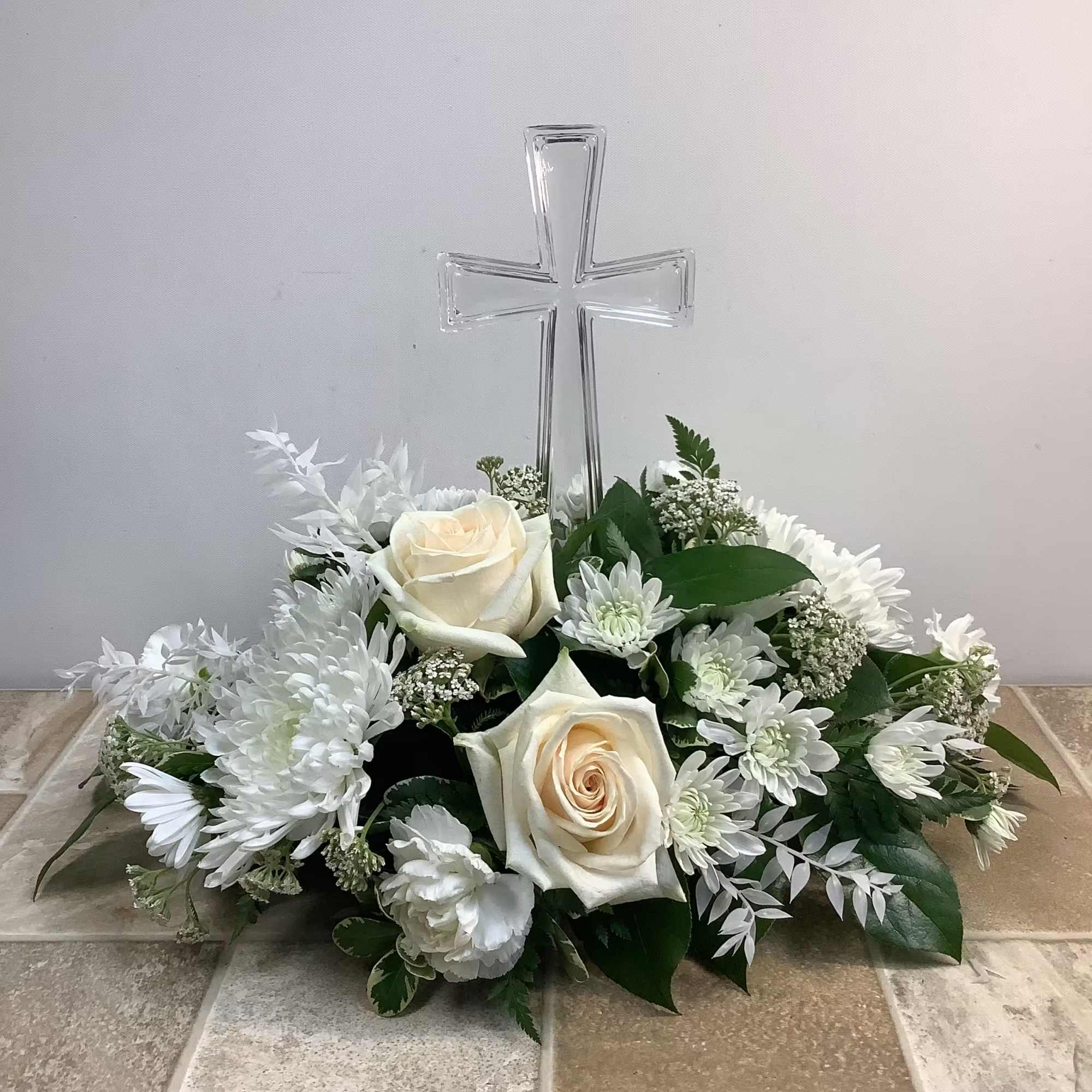 White floral arrangement with roses and daisies beneath a clear cross