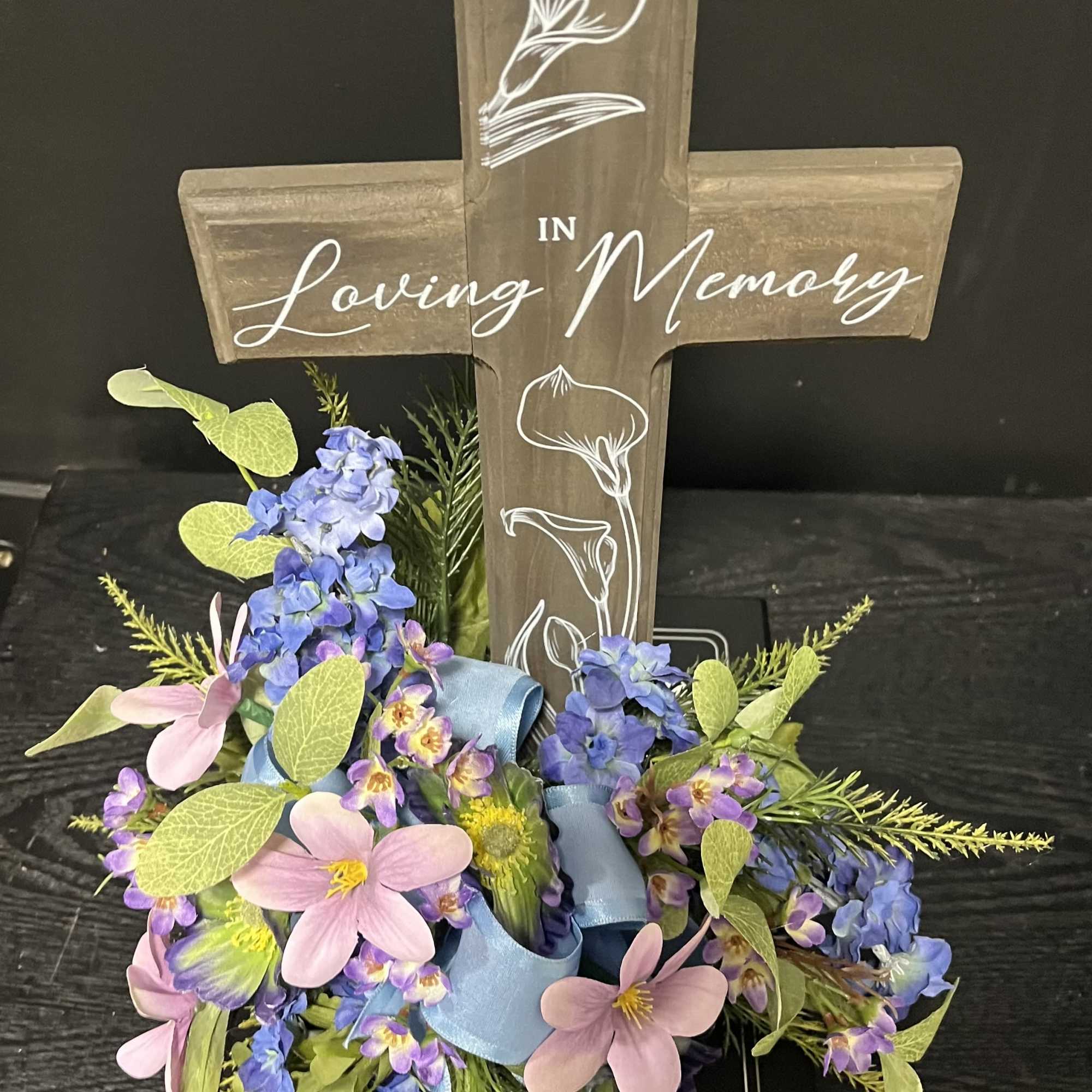 Floral tribute around a wooden cross reading "Loving Memory"