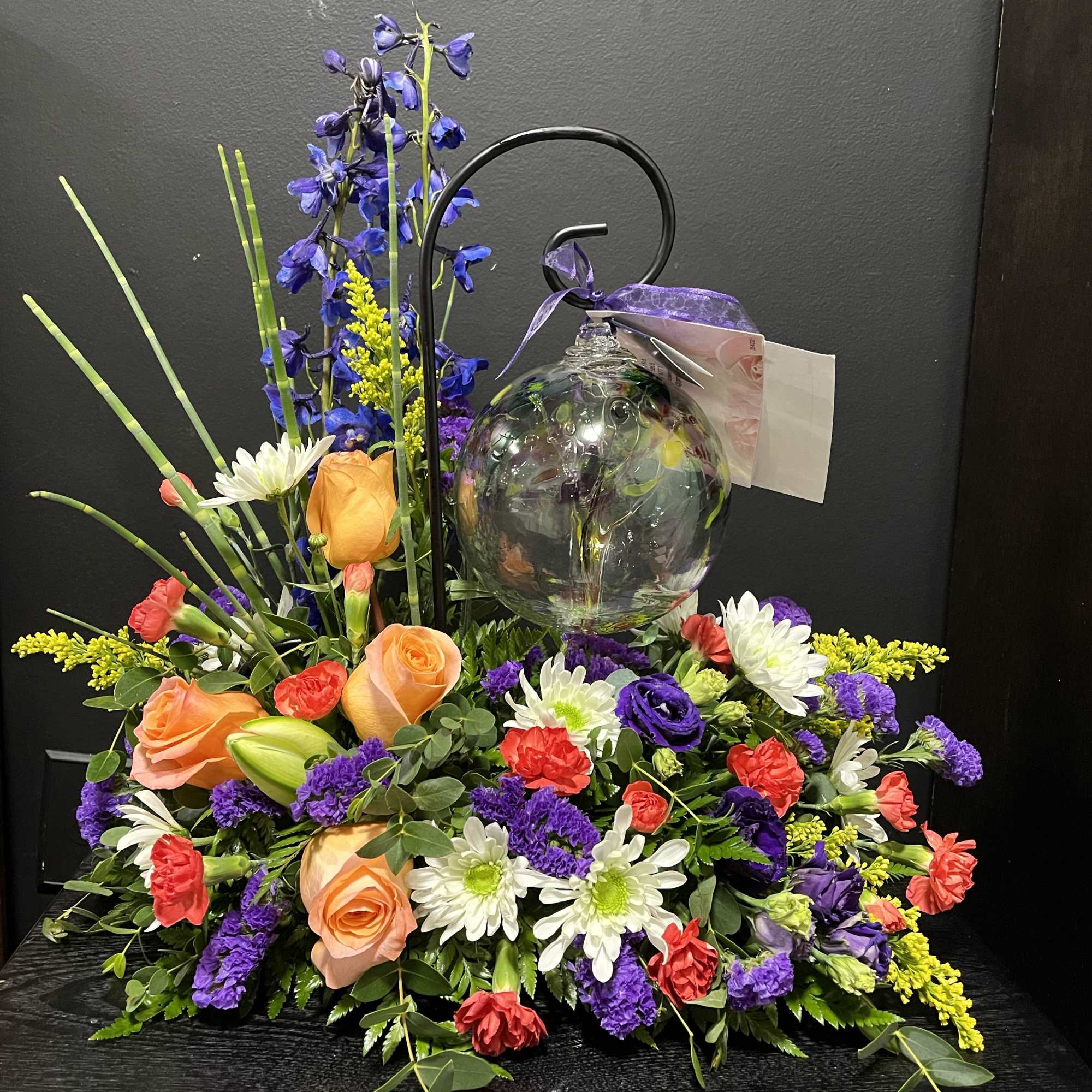 Colorful floral arrangement with roses, daisies, and a glass ornament