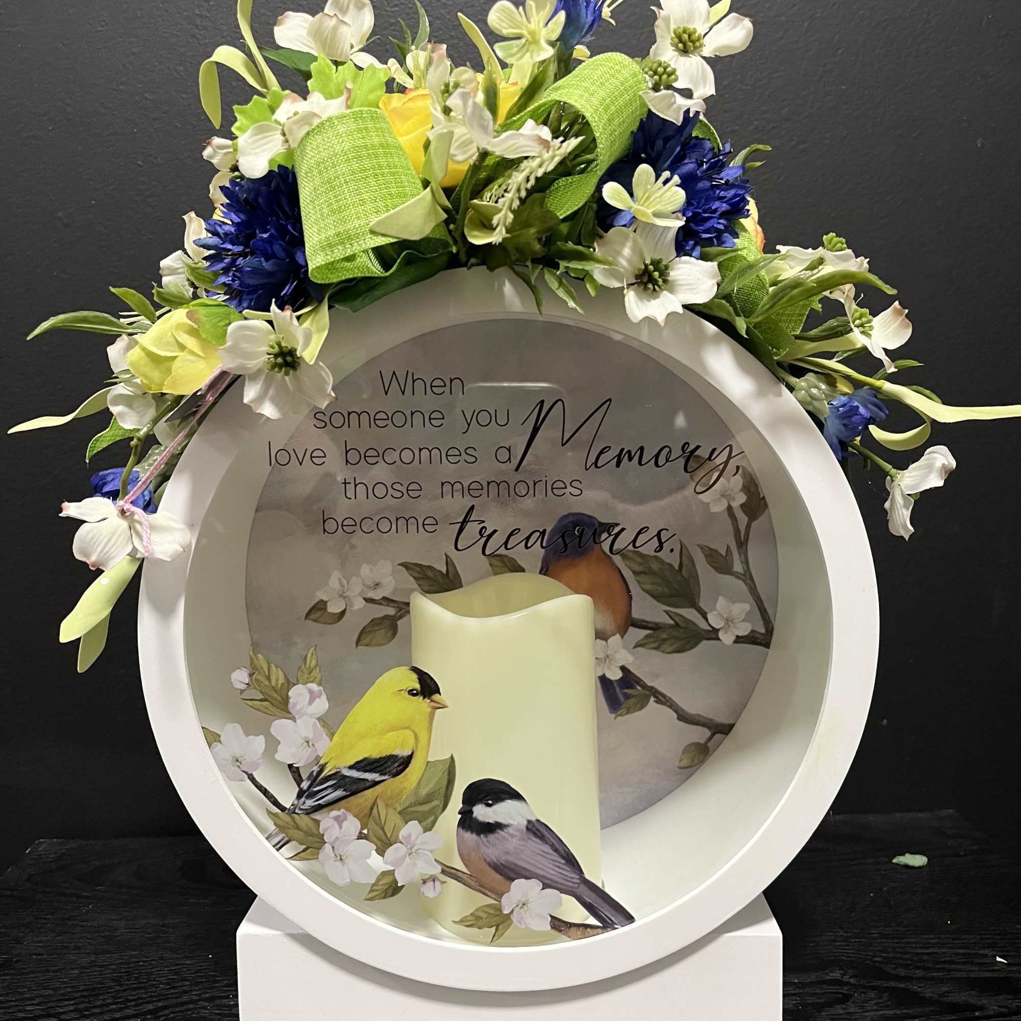 Memorial candle display with a floral wreath and bird illustration