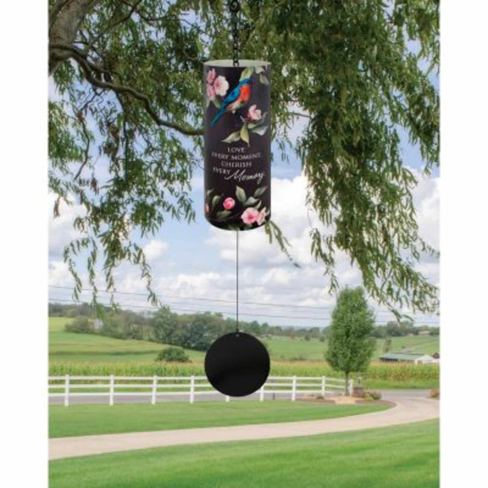 Black memorial wind chime hanging from a tree branch in a rural yard