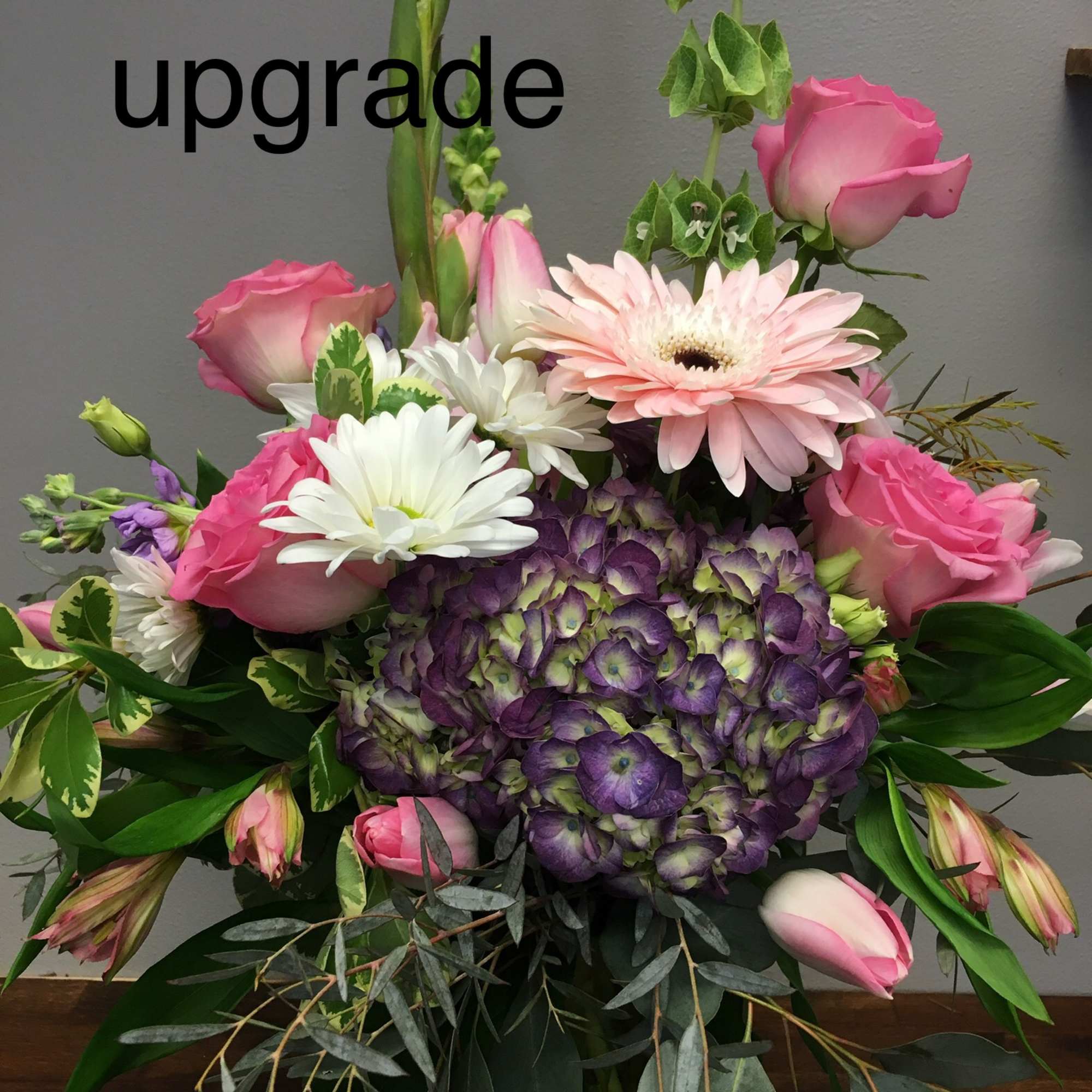 Pink roses and daisies arranged with a purple hydrangea centerpiece