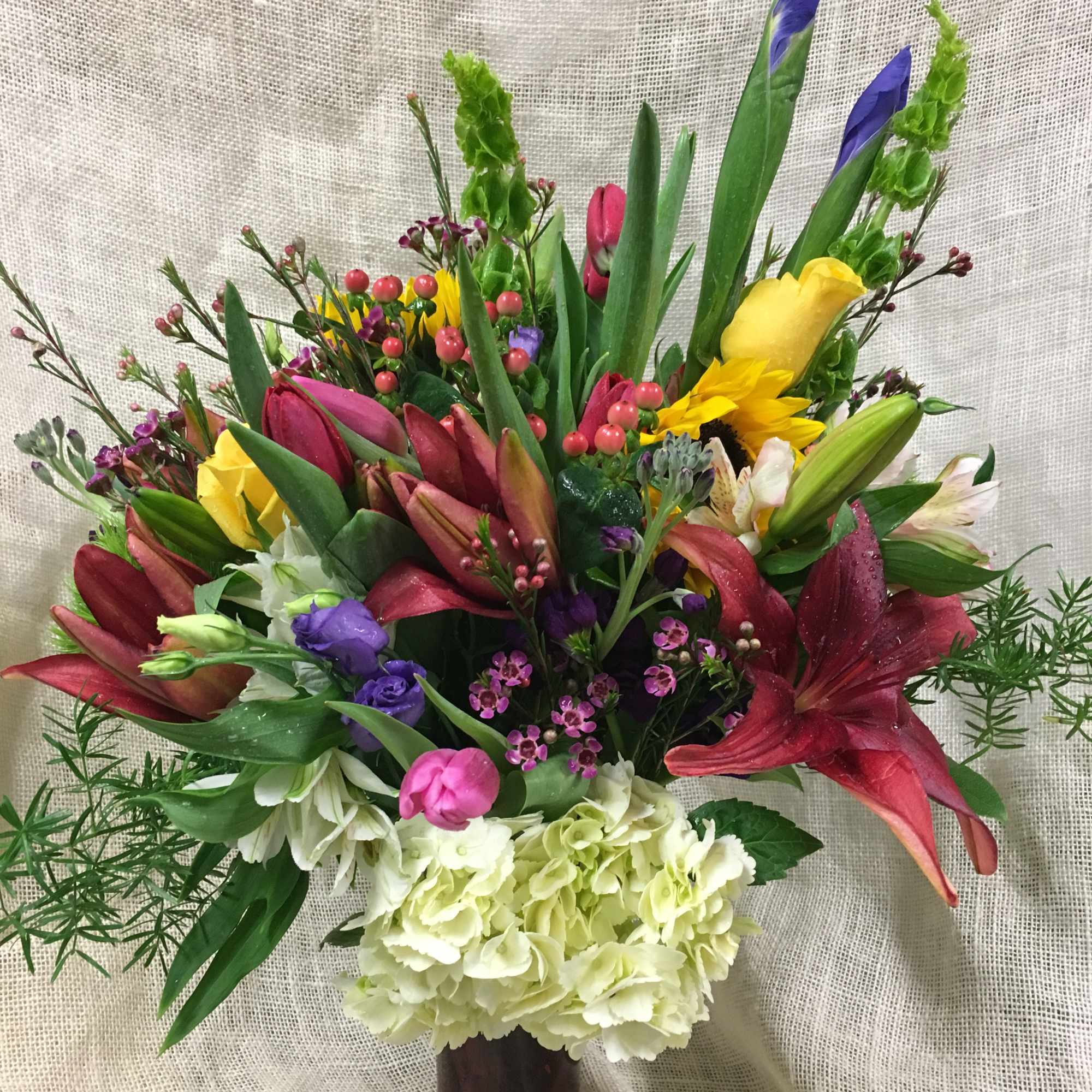 Mixed bouquet with lilies, tulips, sunflowers, and hydrangeas in a glass vase