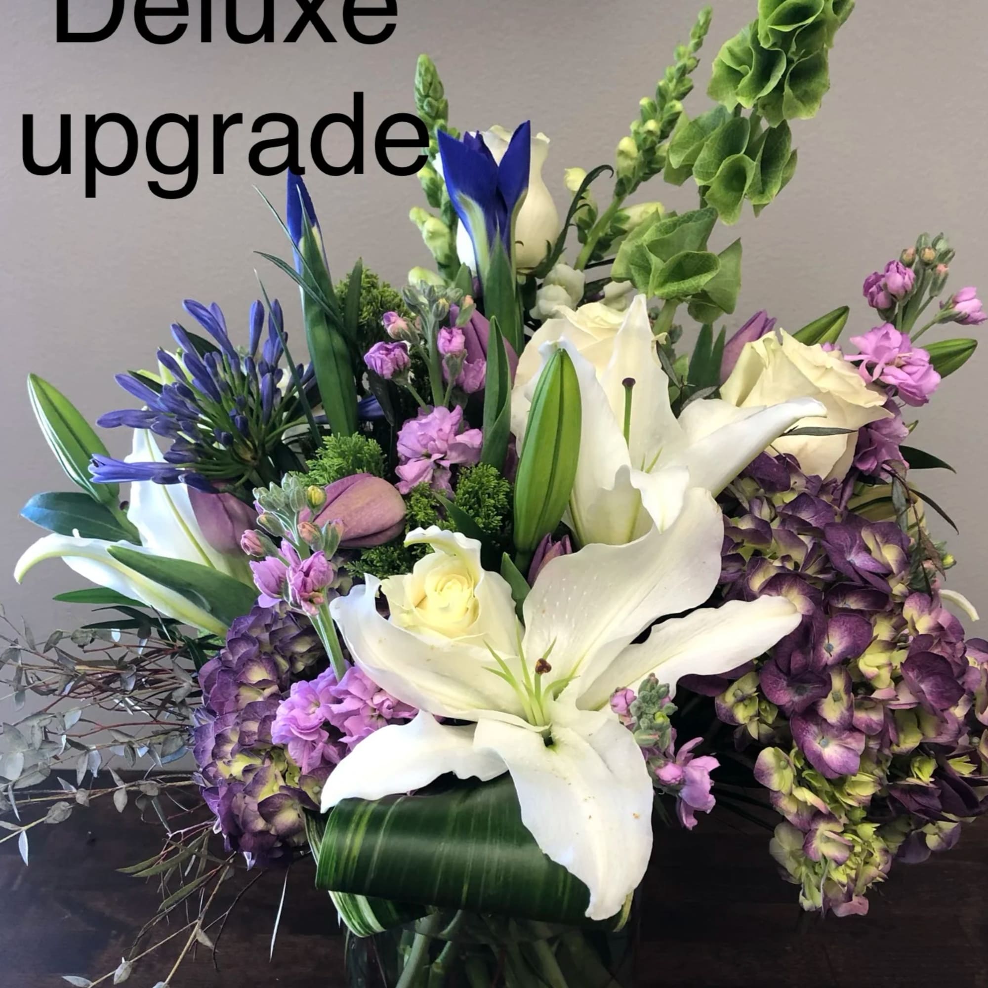 Bouquet of white lilies, purple hydrangeas, and blue flowers in a glass vase