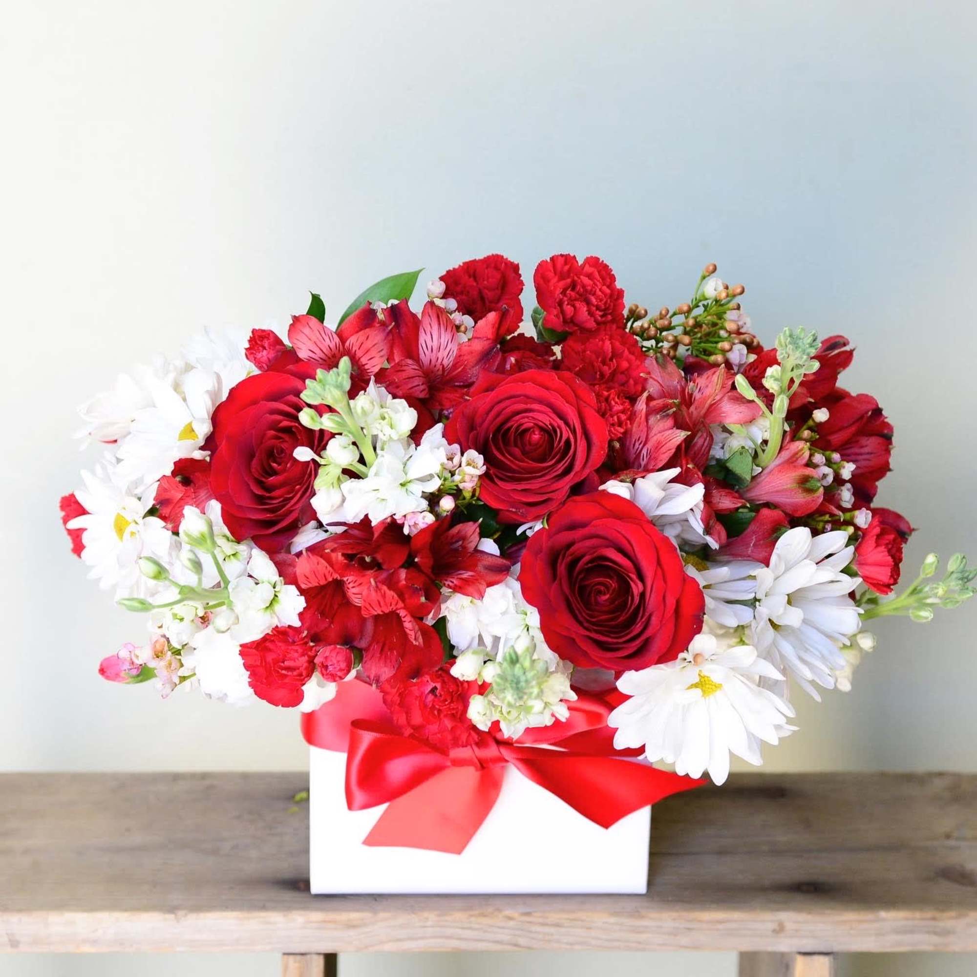 Red roses and white daisies in a white box with a red ribbon