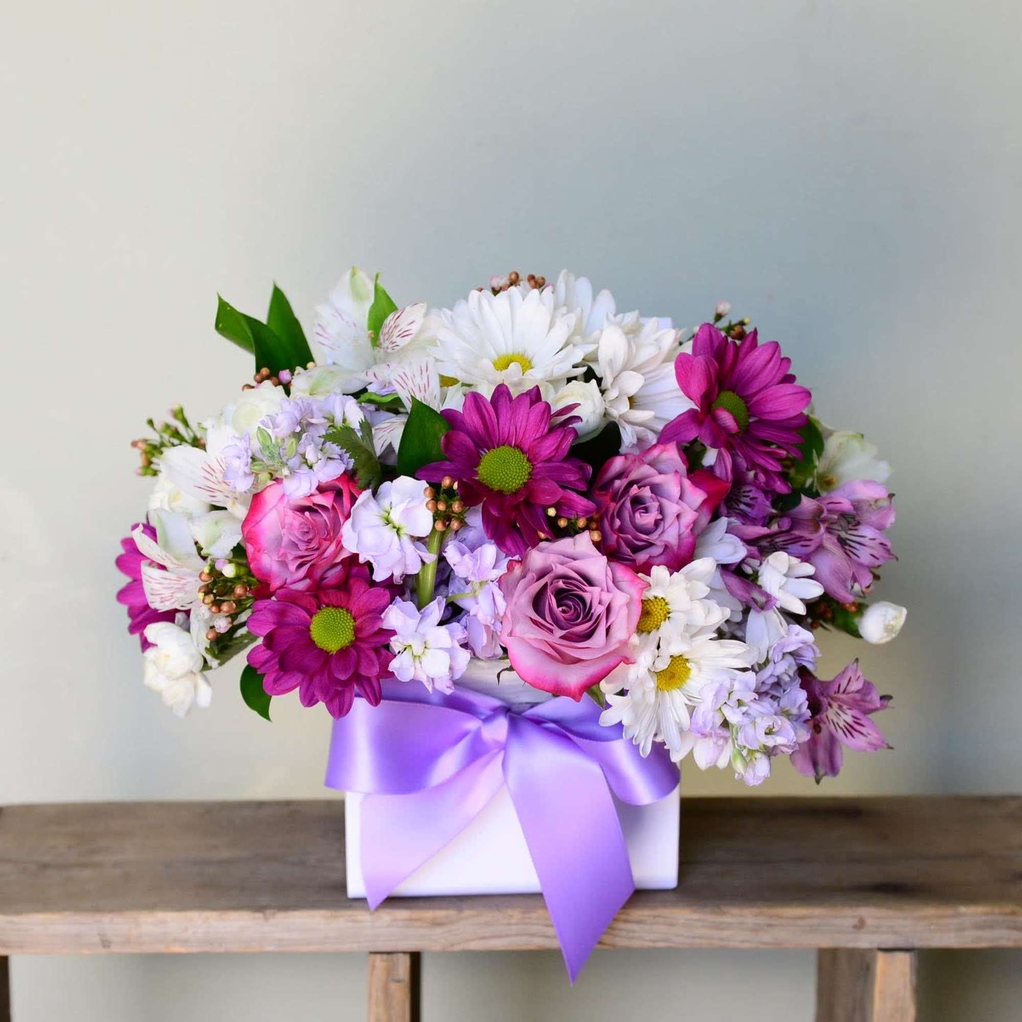 Pink and white mixed flower arrangement in a white box with a purple ribbon