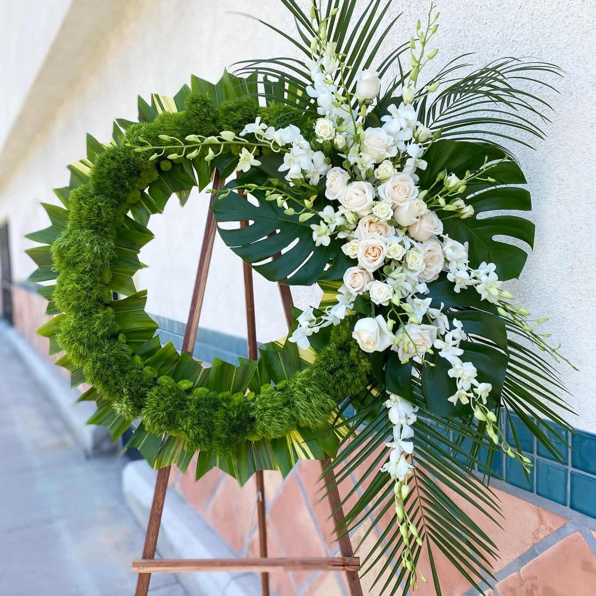 24" wreath covered in tropical green leaves. The flowers are roses and